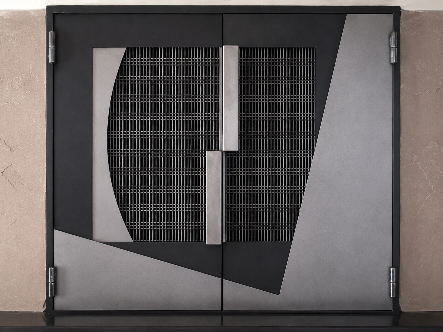 Double metal doors with black and gray geometric design, mesh grilles, and metallic handles, set against a brown textured wall.