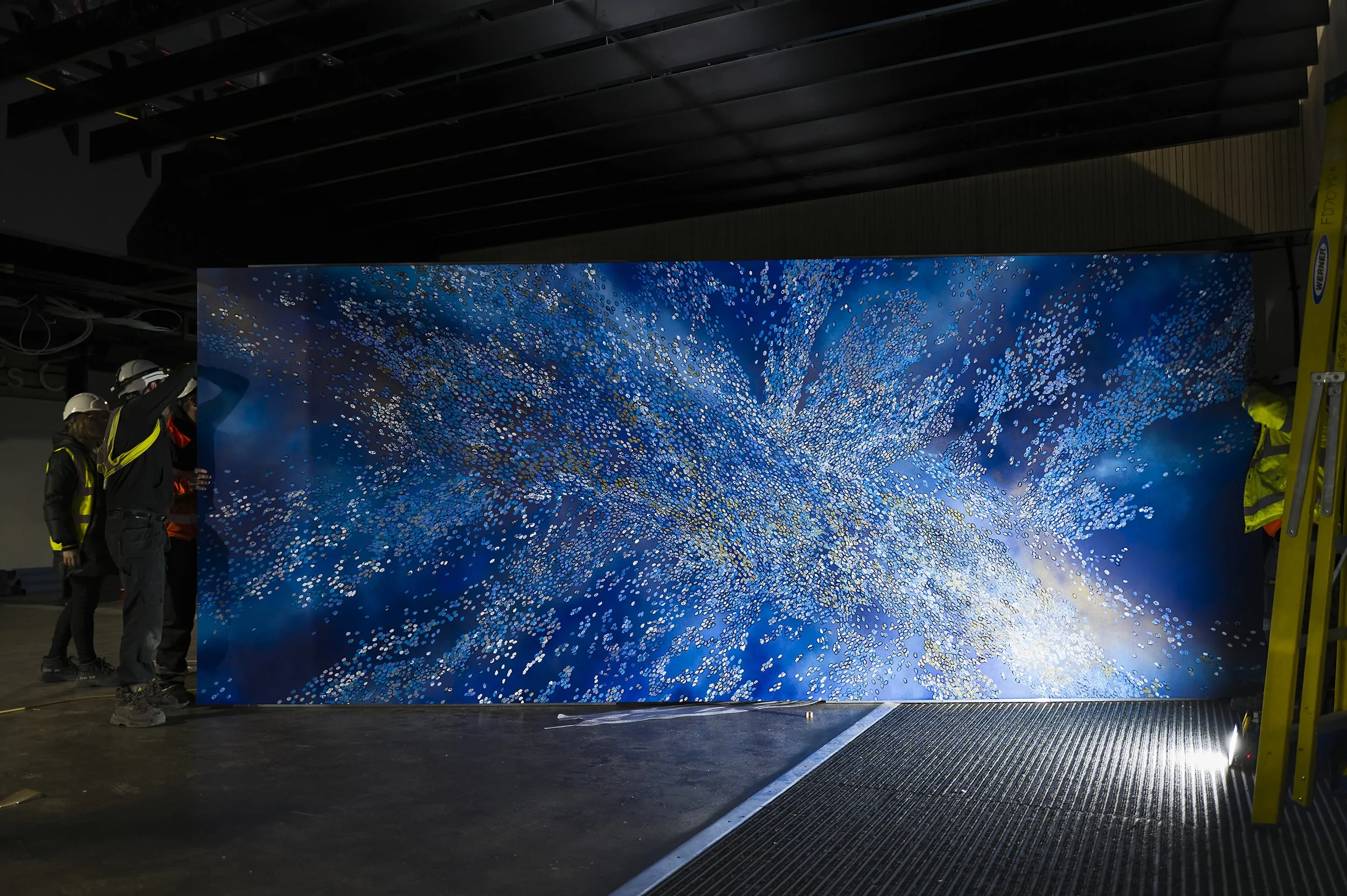 Group of workers installing a large digital display with abstract blue and white patterns in an indoor setting.
