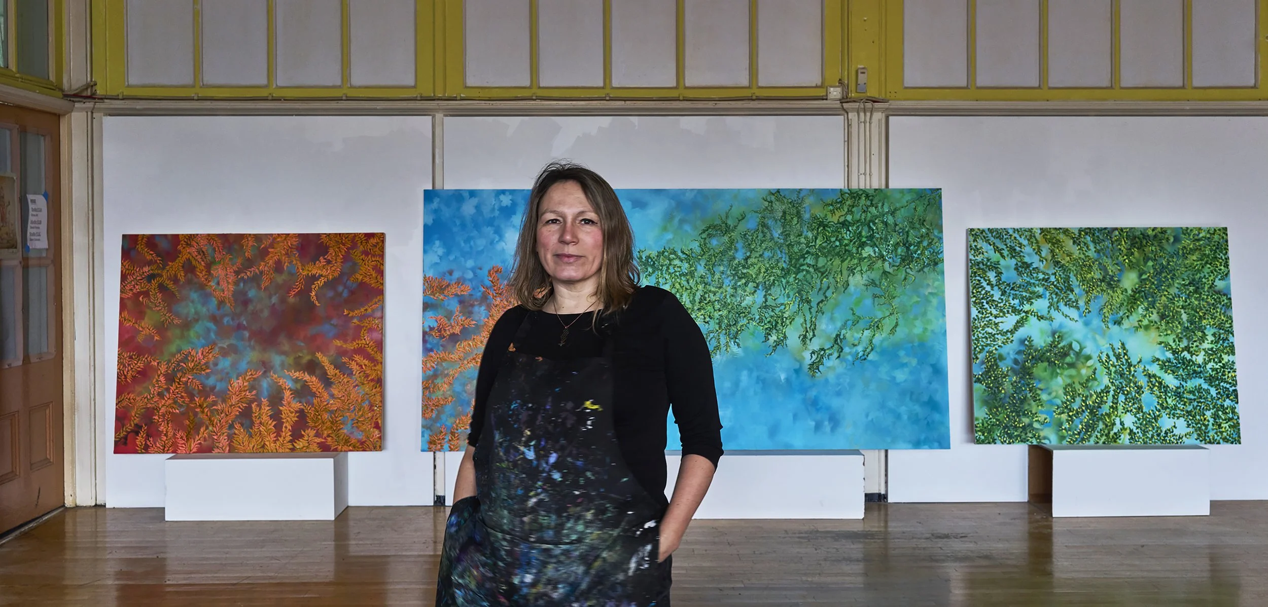 Female artist standing in front of colorful abstract paintings in an art gallery.