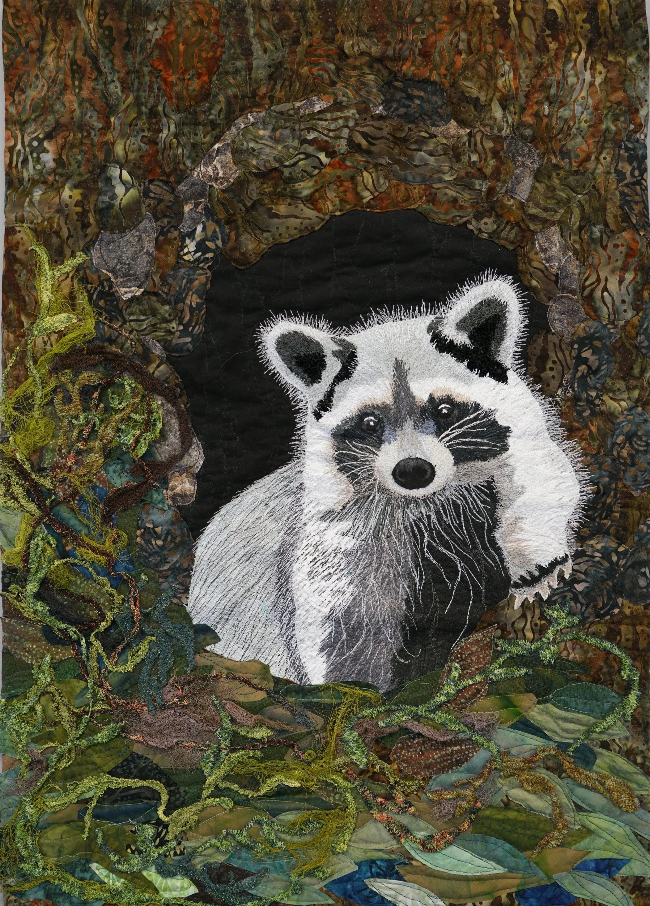 Trouble: Trouble, a fiber art quilt by Janet Fox depicting a raccoon surrounded by richly textured and stitched woodland elements.