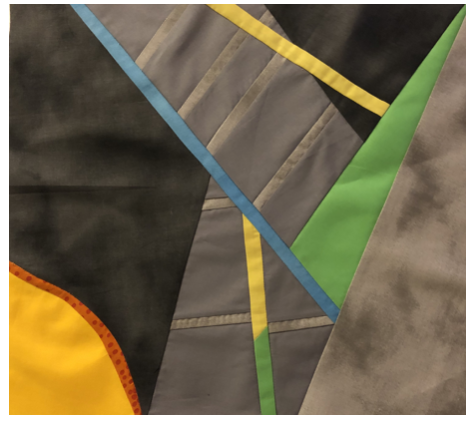 Close-up of a colorful fabric with black, green, blue, yellow, gray, and orange sections, possibly part of a piece of art or clothing.