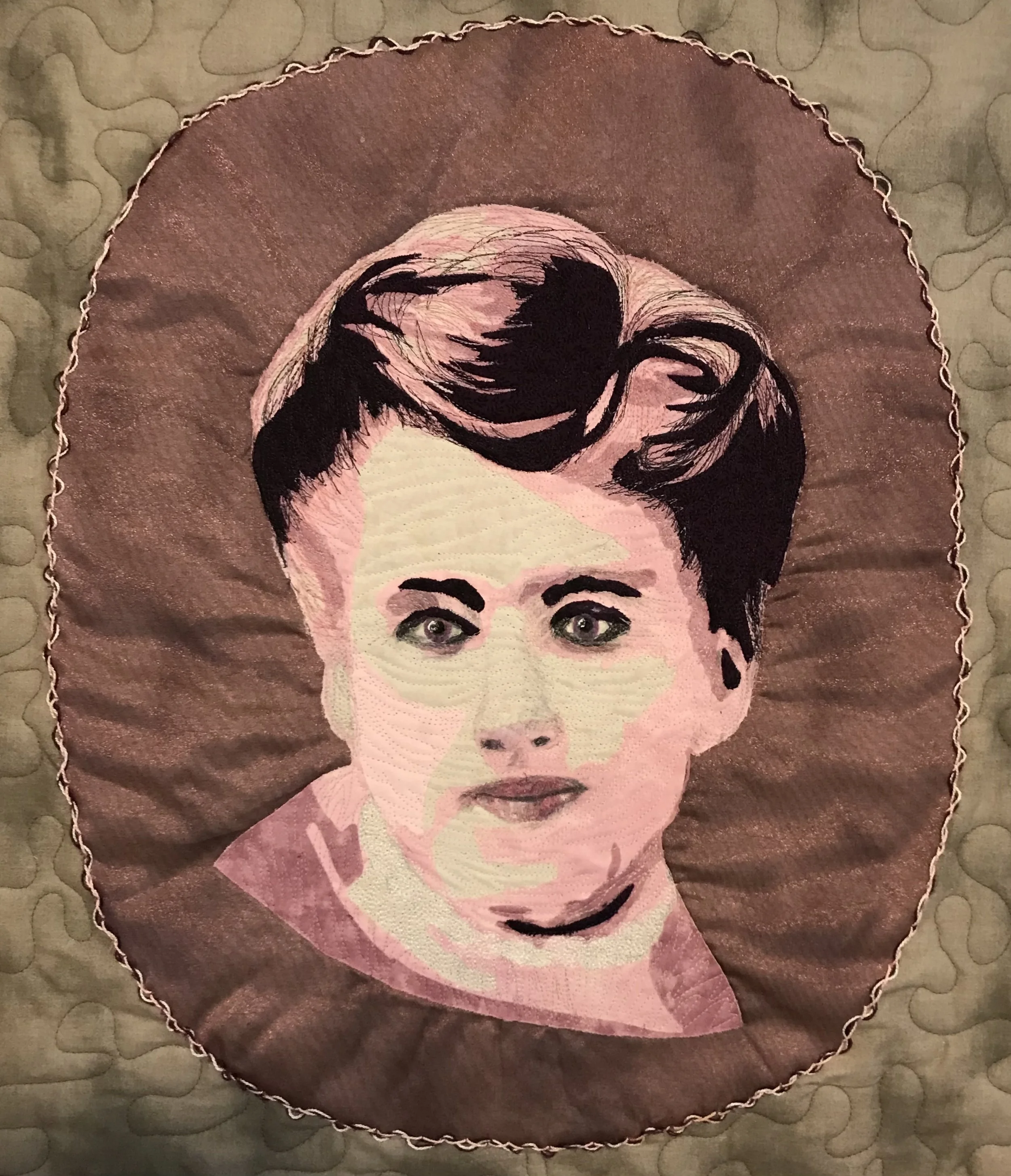 Embroidery of a woman's face with short hair and earrings on a round, scalloped-edge fabric piece.
