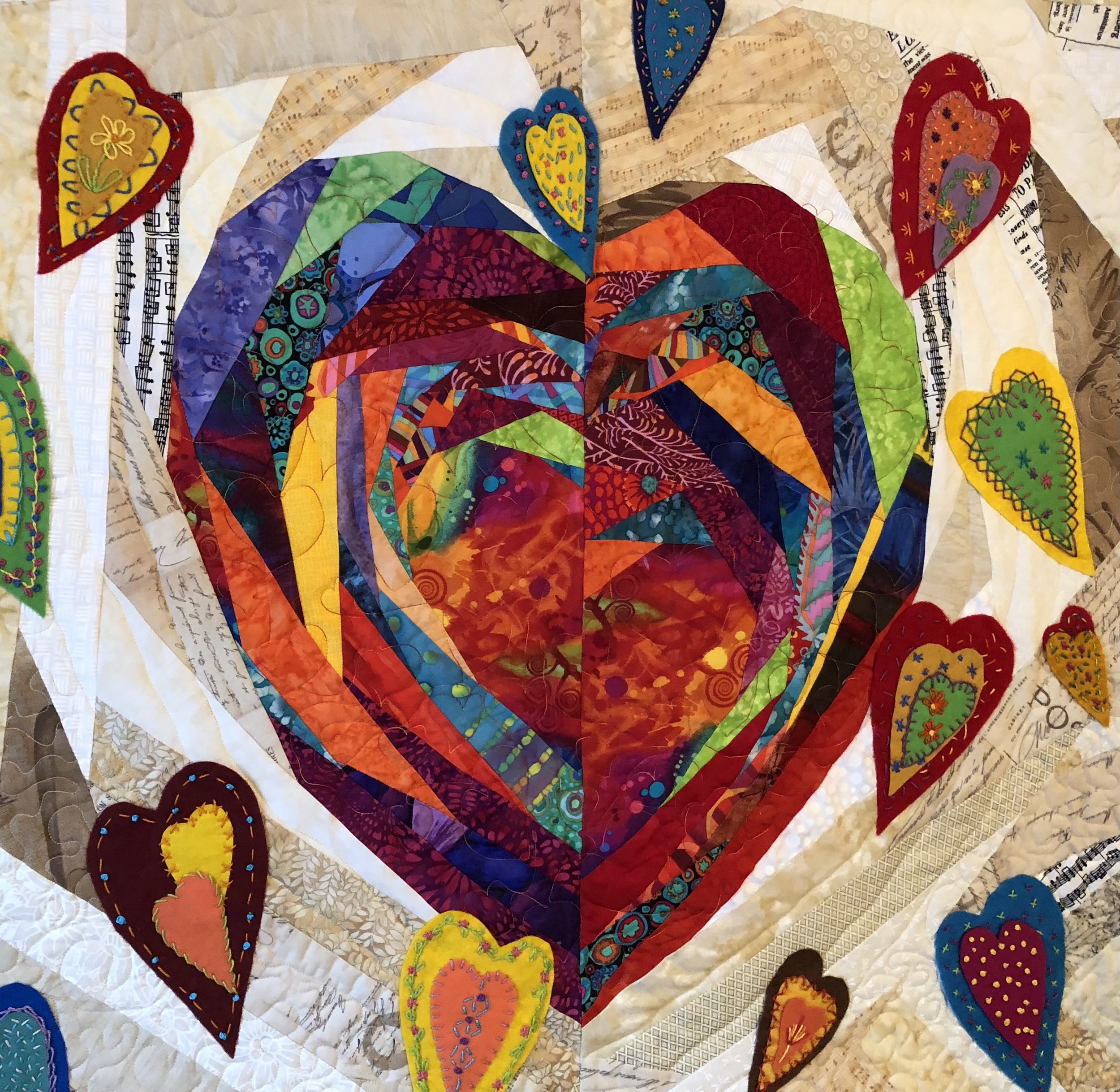 Colorful fabric quilt with heart-shaped appliques and various patterned fabrics, with patches of handwritten script and musical notation in the background.