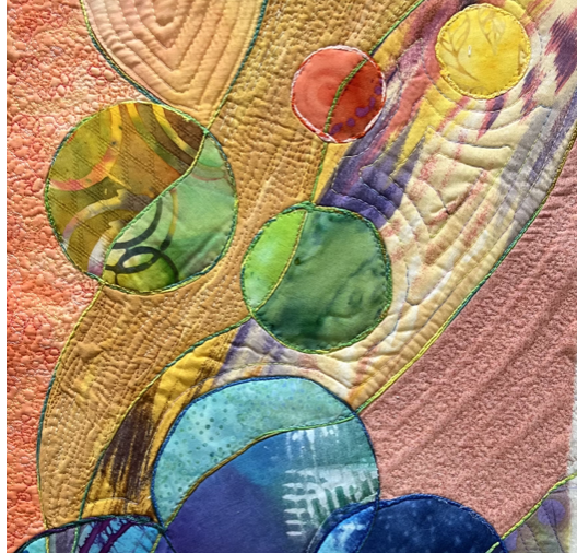 Close-up of a colorful, abstract quilt with circular patterns in various bright colors and stitching details.