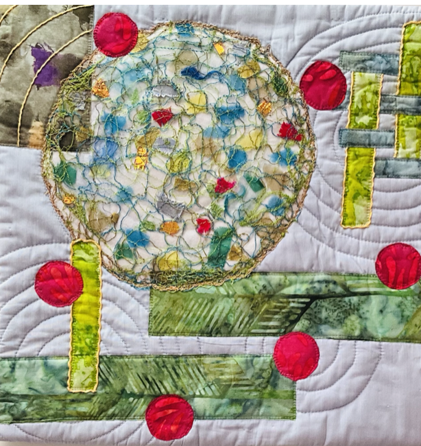 Close-up of a quilt featuring a colorful, circular embroidered design with green, yellow, and blue threads, surrounded by red circular embellishments and green fabric patches.