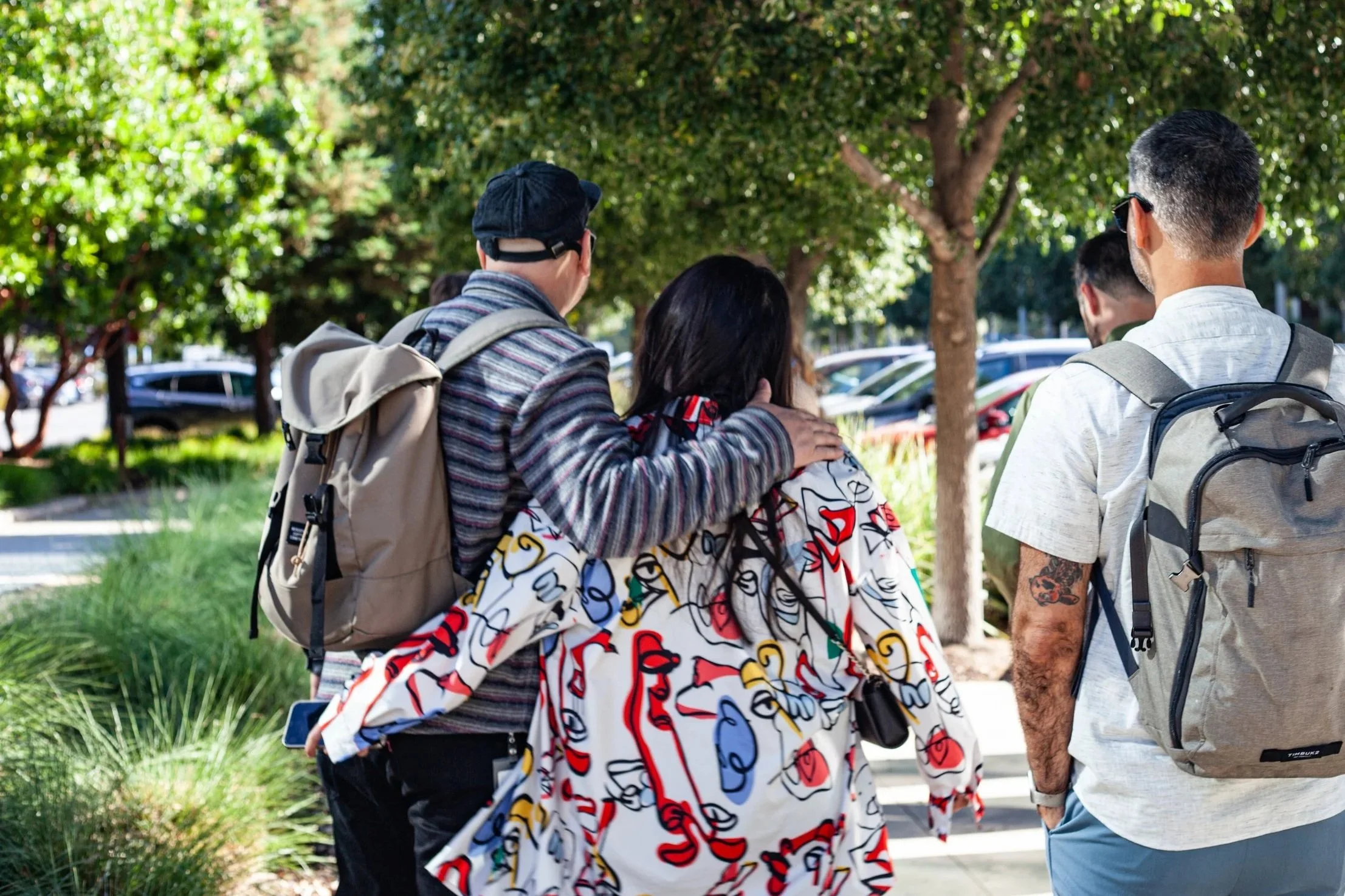 Group of world class creatives walking outdoors on a sunny day at Intuit, with lush green trees and parked cars in the background.