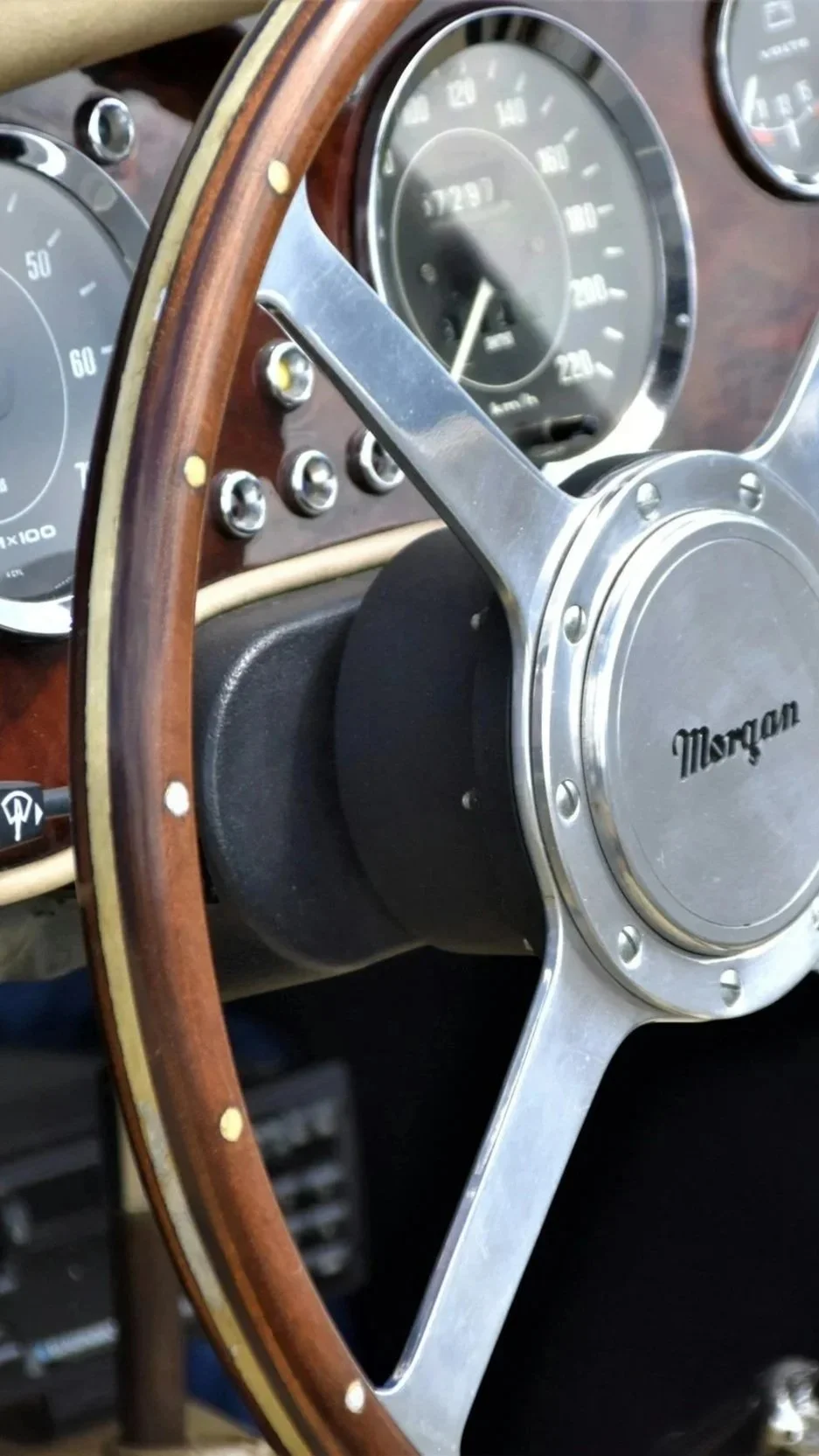 Close-up of a vintage Morgan wooden steering wheel and dashboard with analog gauges.