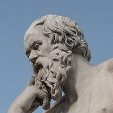 Close-up of a classical marble statue of Socrates with a thoughtful expression against a clear blue sky.