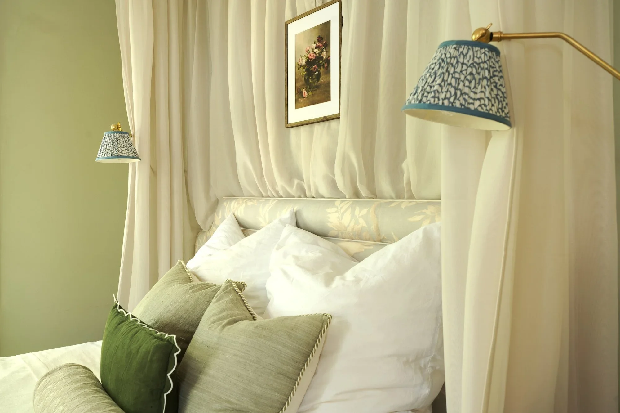 Linen pillows, a dark green scalloped cushion and a bolster against a Lewis & Wood Doves headboard, under a sheer bed canopy