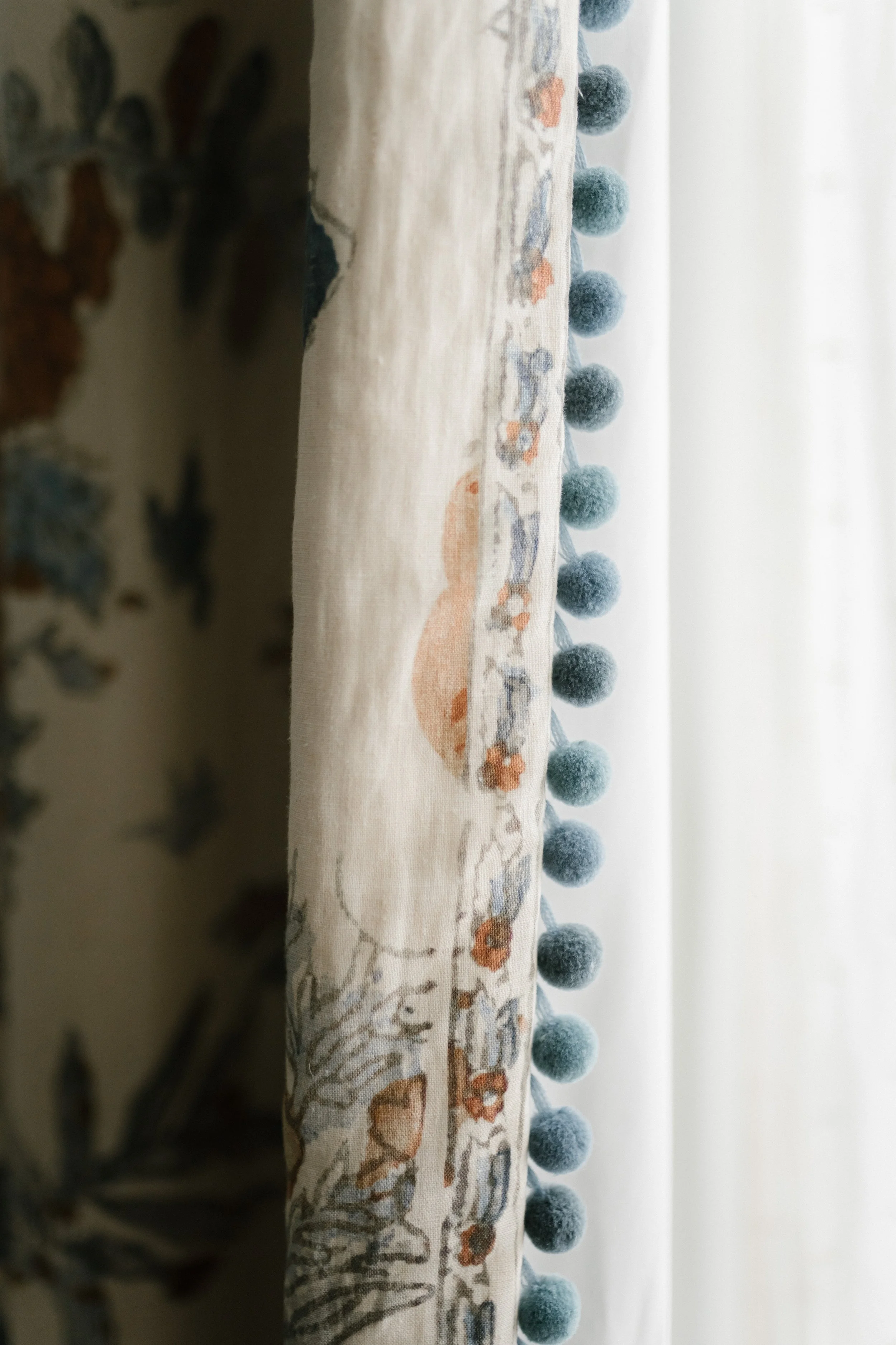 Detail of a linen curtain edged with blue pom-pom trim, from an English country house scheme