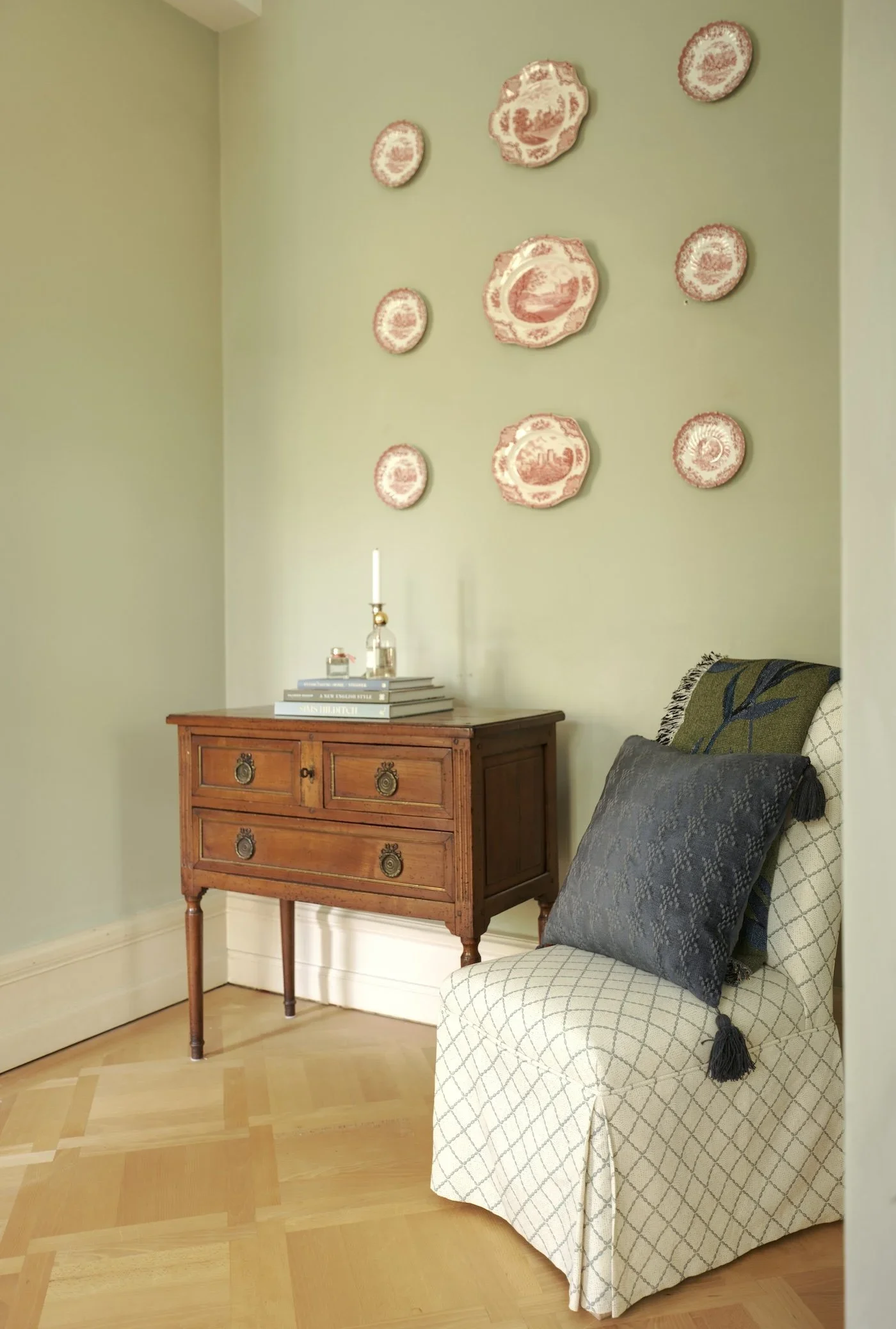 Raspberry transferware plates hung in a grid on Farrow & Ball French Gray walls, above an antique chest of drawers
