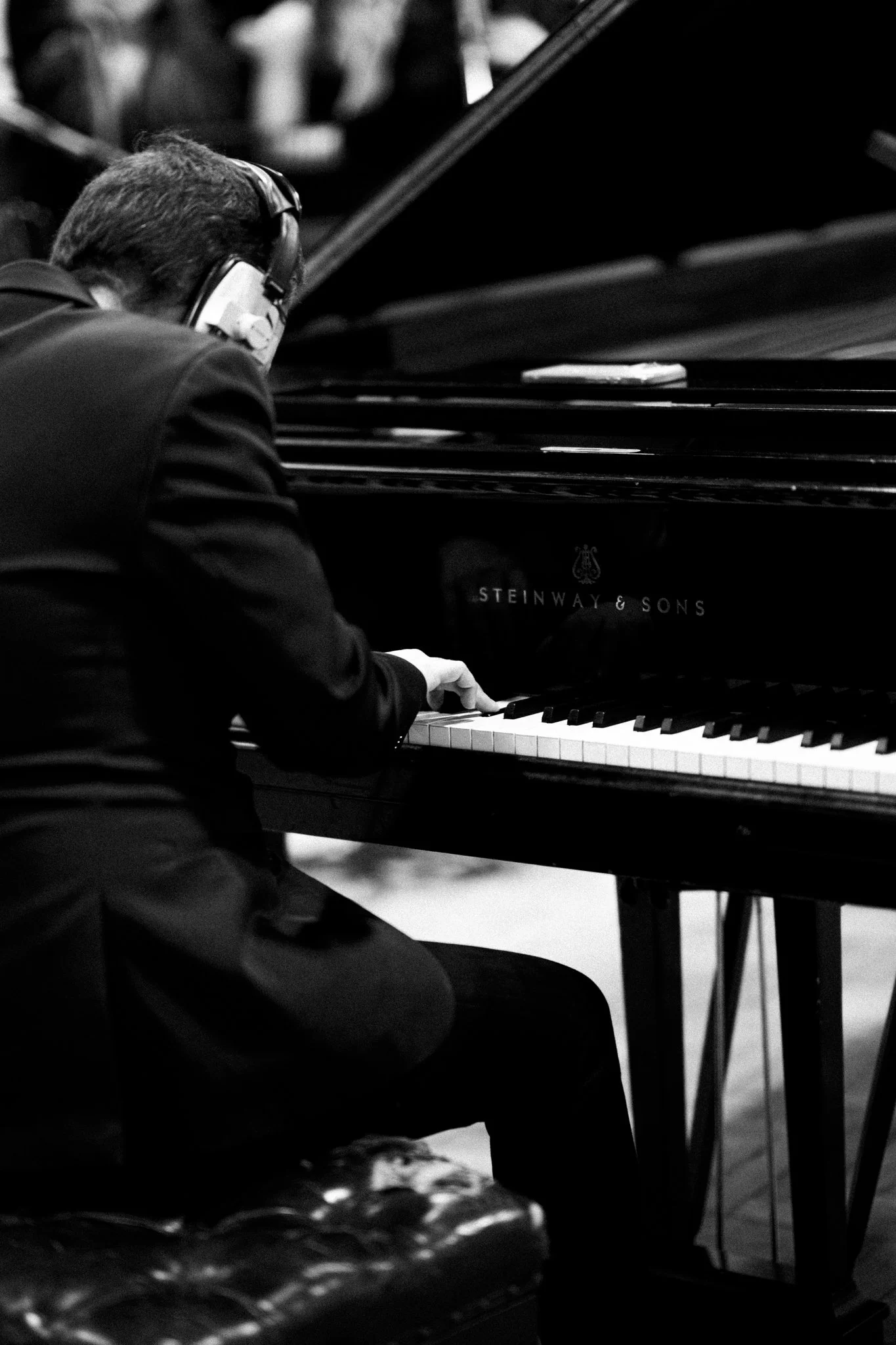 A person wearing headphones is playing a grand piano in a dimly lit room.
