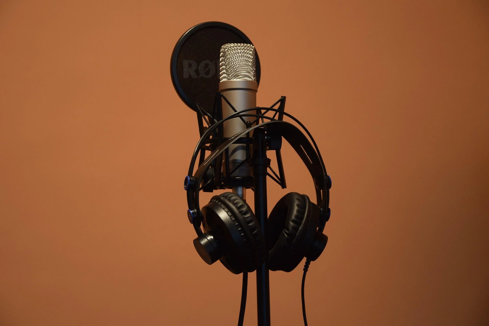 A professional recording microphone surrounded by headphones hanging on a stand.