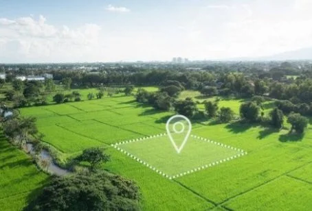 A lush green field with a marked plot of land outlined by dotted lines, adjacent to a small waterway, with a cloudy sky overhead.