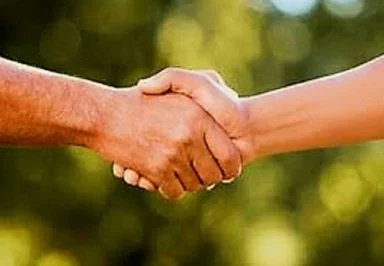 Two people shaking hands outdoors with a blurred green background.