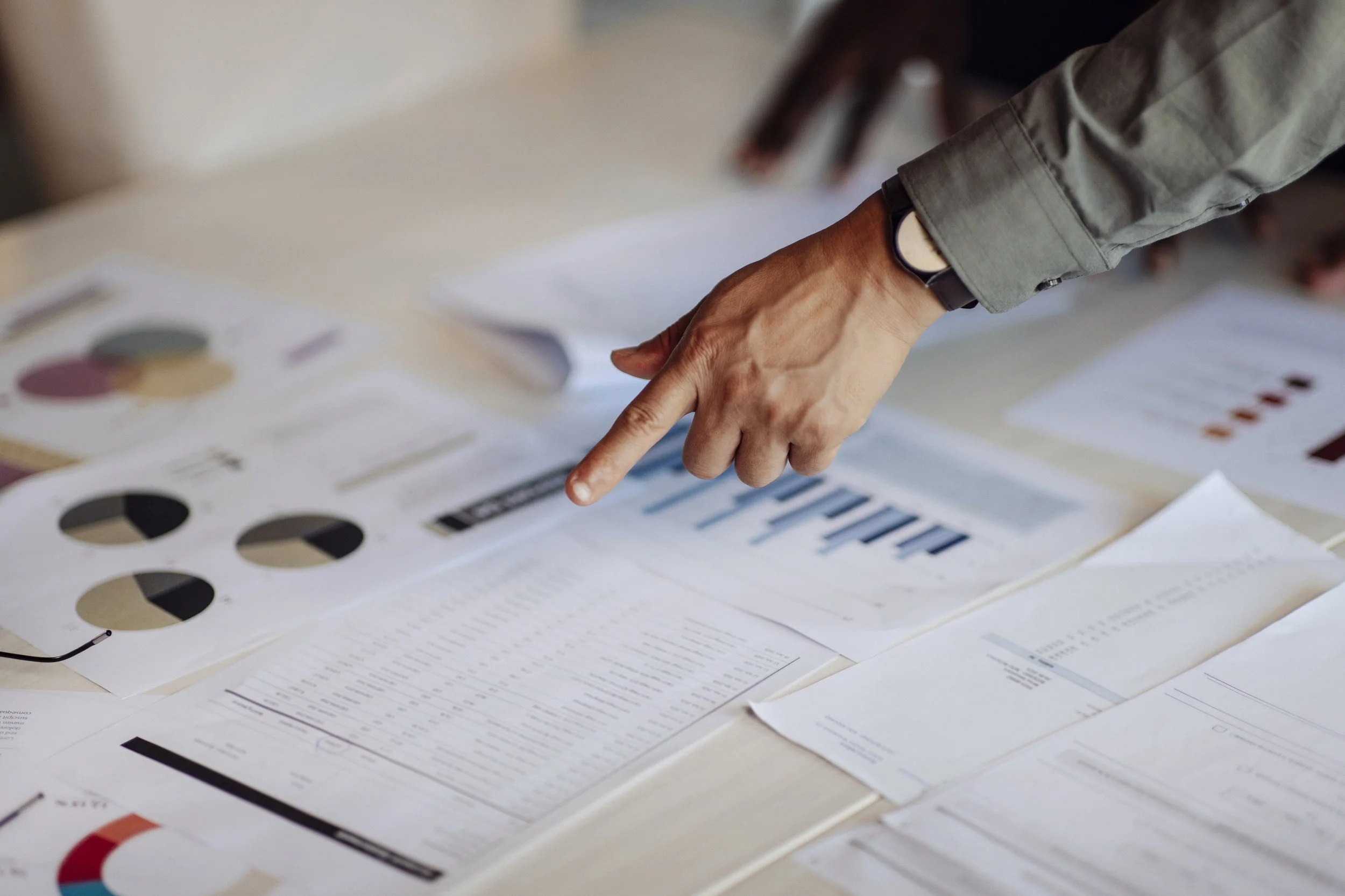 Hand pointing to charts and financial reports during a business performance review.