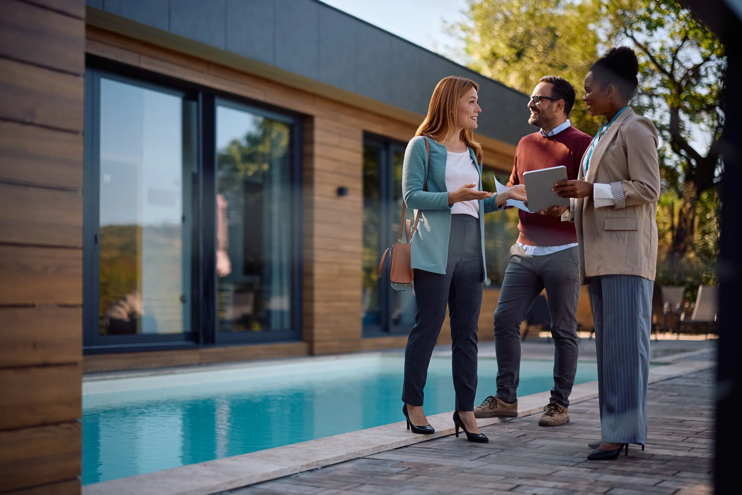 Three people discussing a residential property outside a modern home.