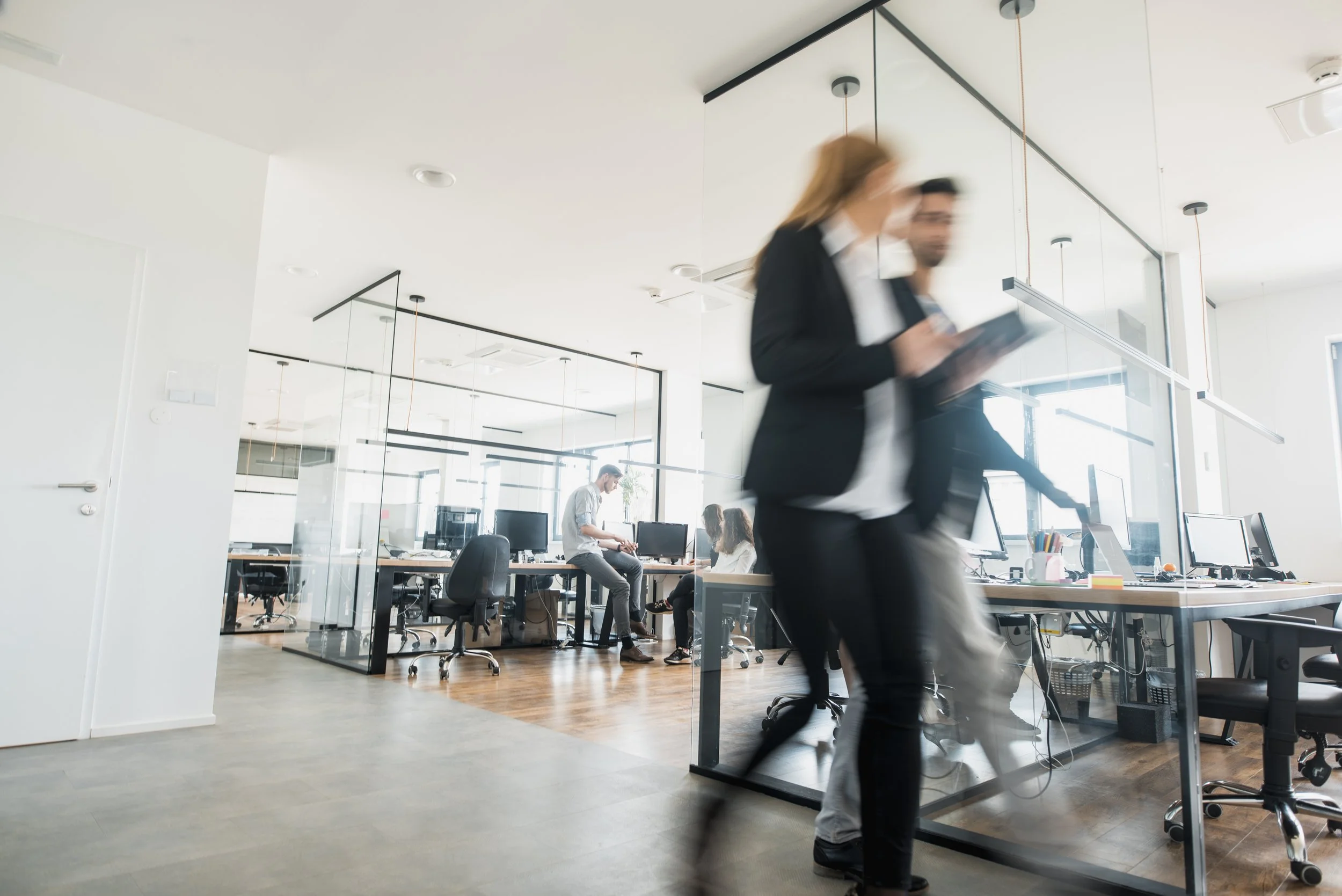 Business professionals moving through a busy, modern office workspace.