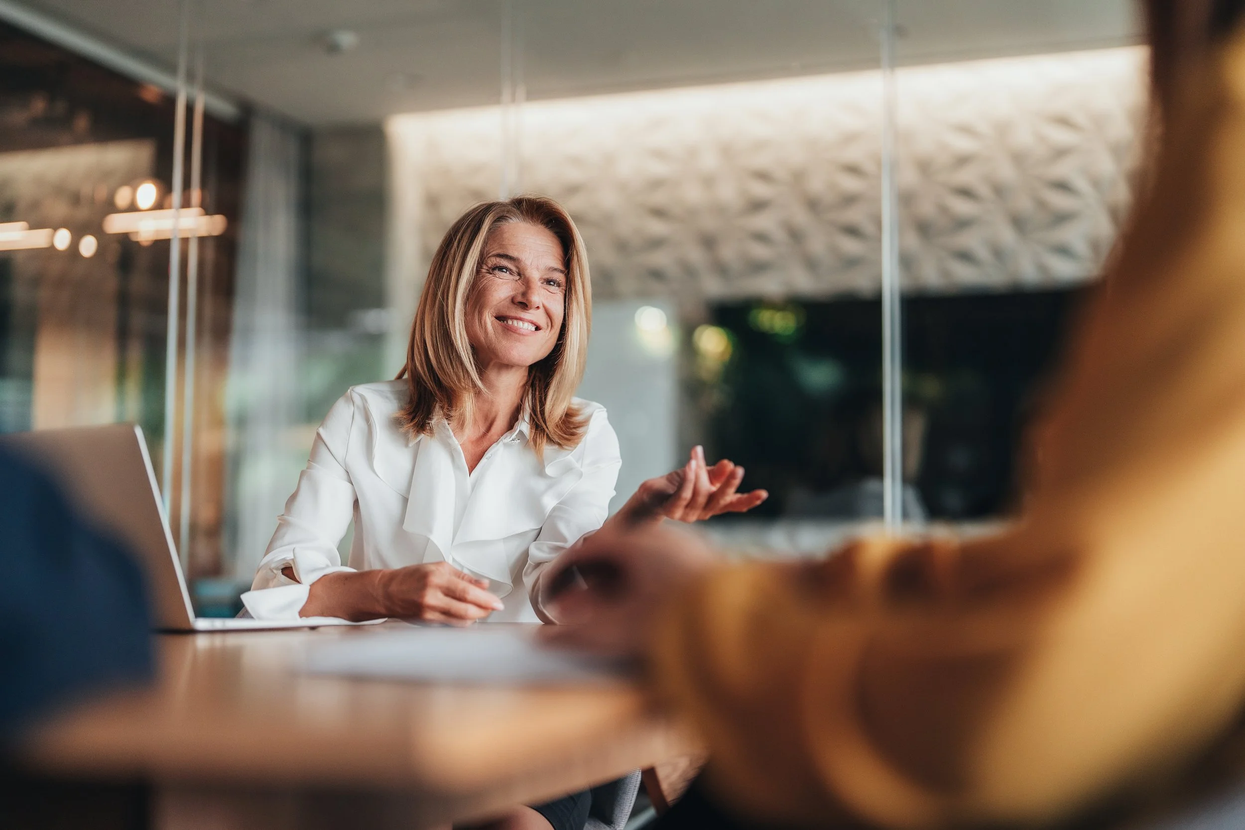 Smiling business professional having a conversation with another person across a table.