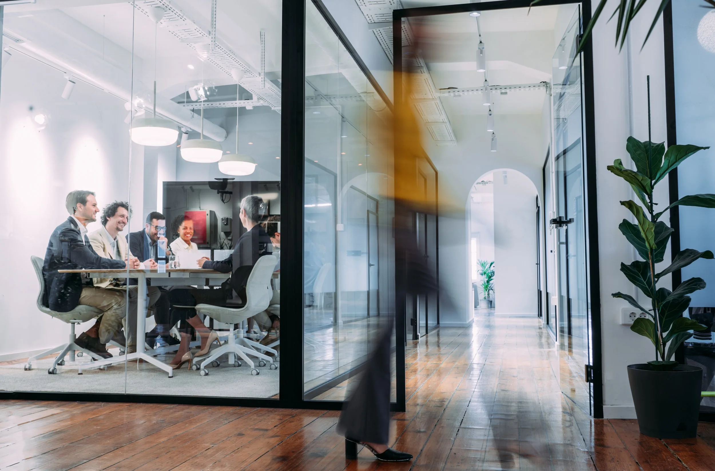 Group of business professionals collaborating around a conference table in a modern glass-walled office.