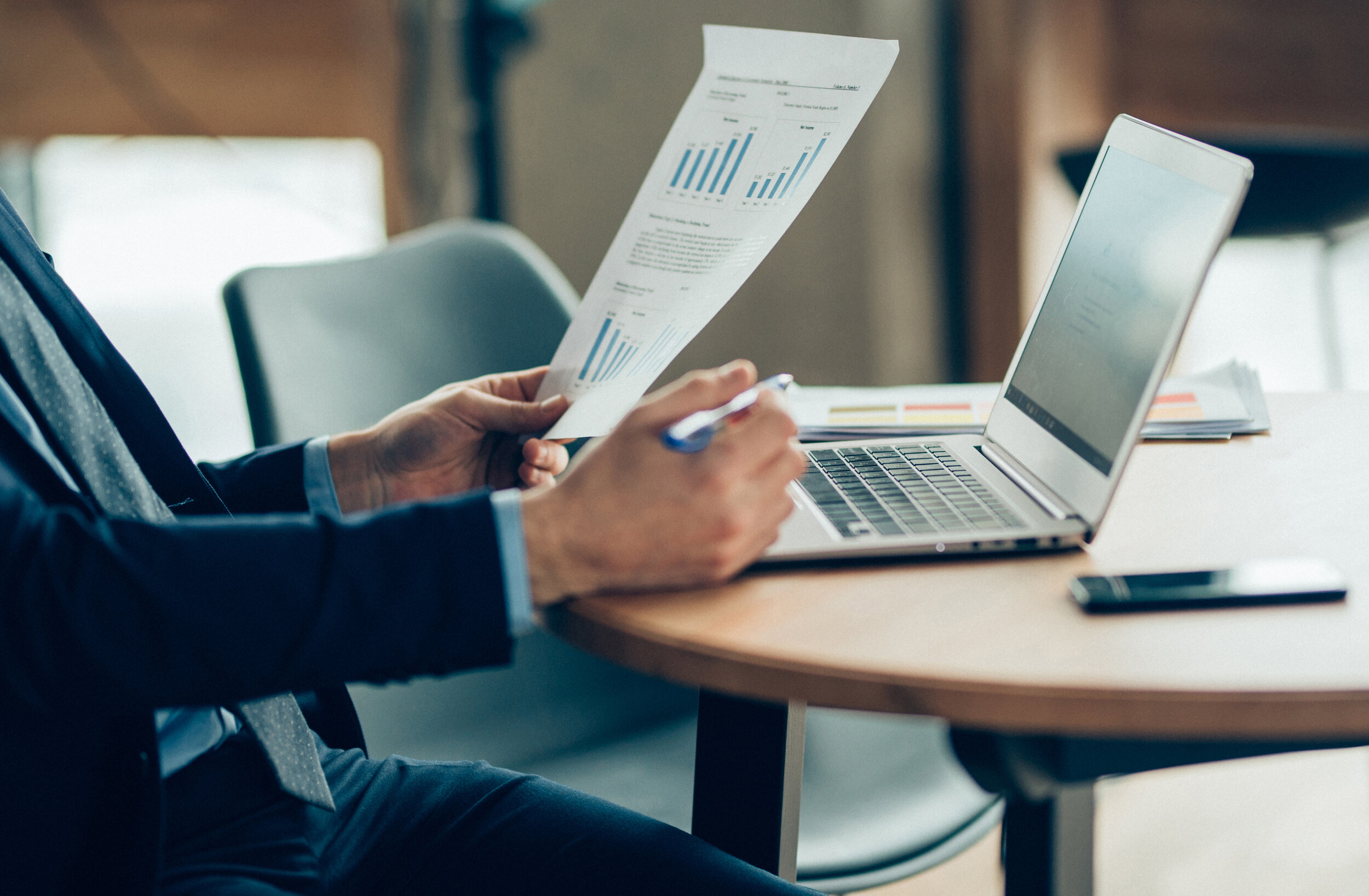 Business professional reviewing financial charts and reports alongside a laptop.