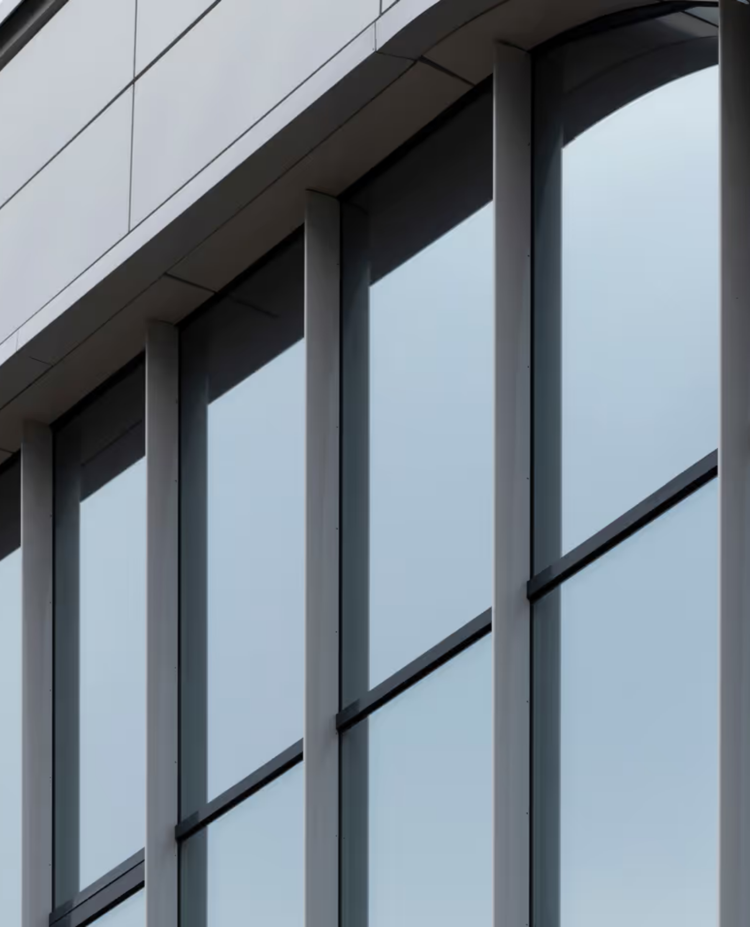 Close-up of a modern building's exterior with large glass windows framed by vertical metal beams and reflective surfaces.