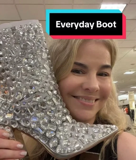 A woman smiling and holding a large, shiny, jeweled high-heeled shoe decorated with numerous rhinestones.