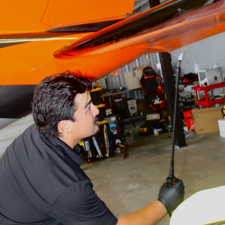 Technician detailing the underside of a Piper PA-46 wing in a hangar