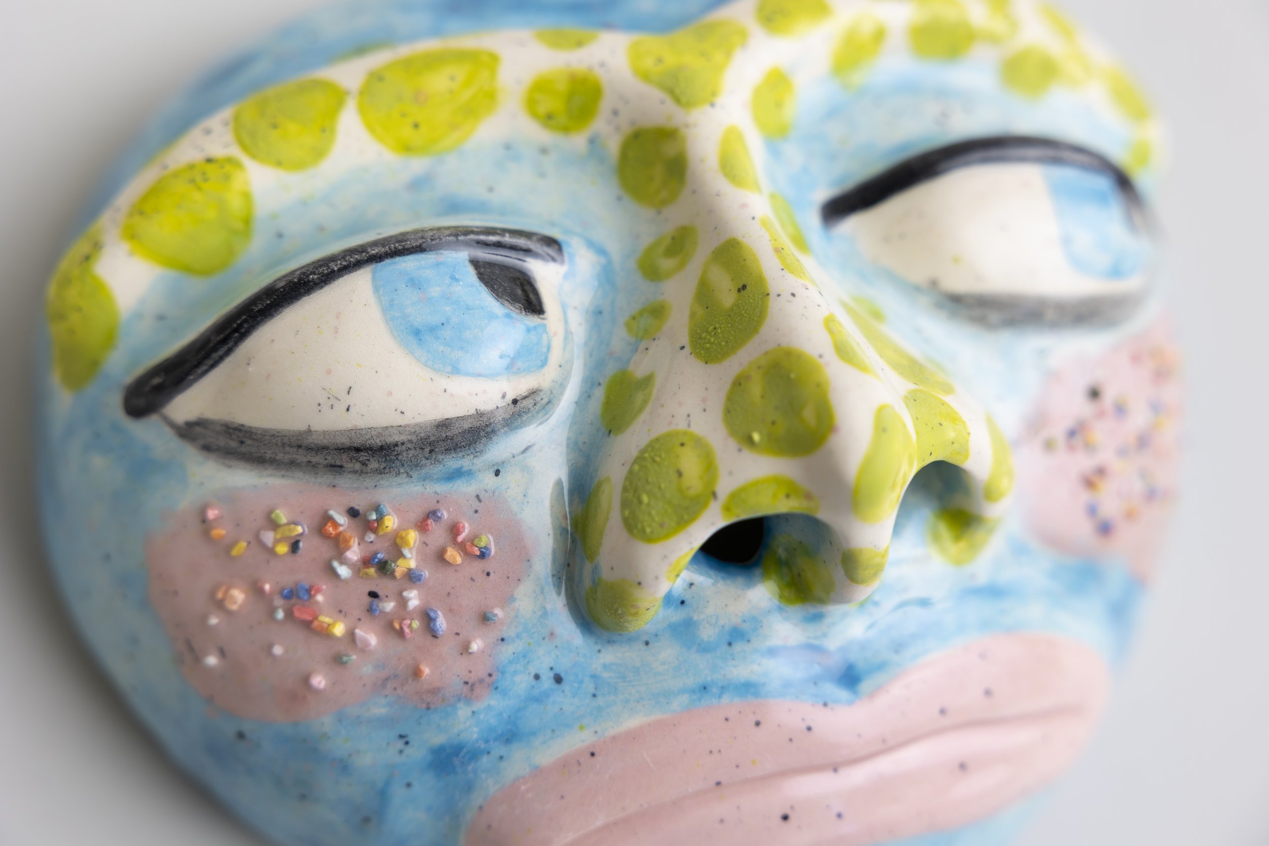 Close-up of a colorful decorative skull with blue, green, pink, and black accents, featuring painted eyes, green dots, and multicolored sprinkles.
