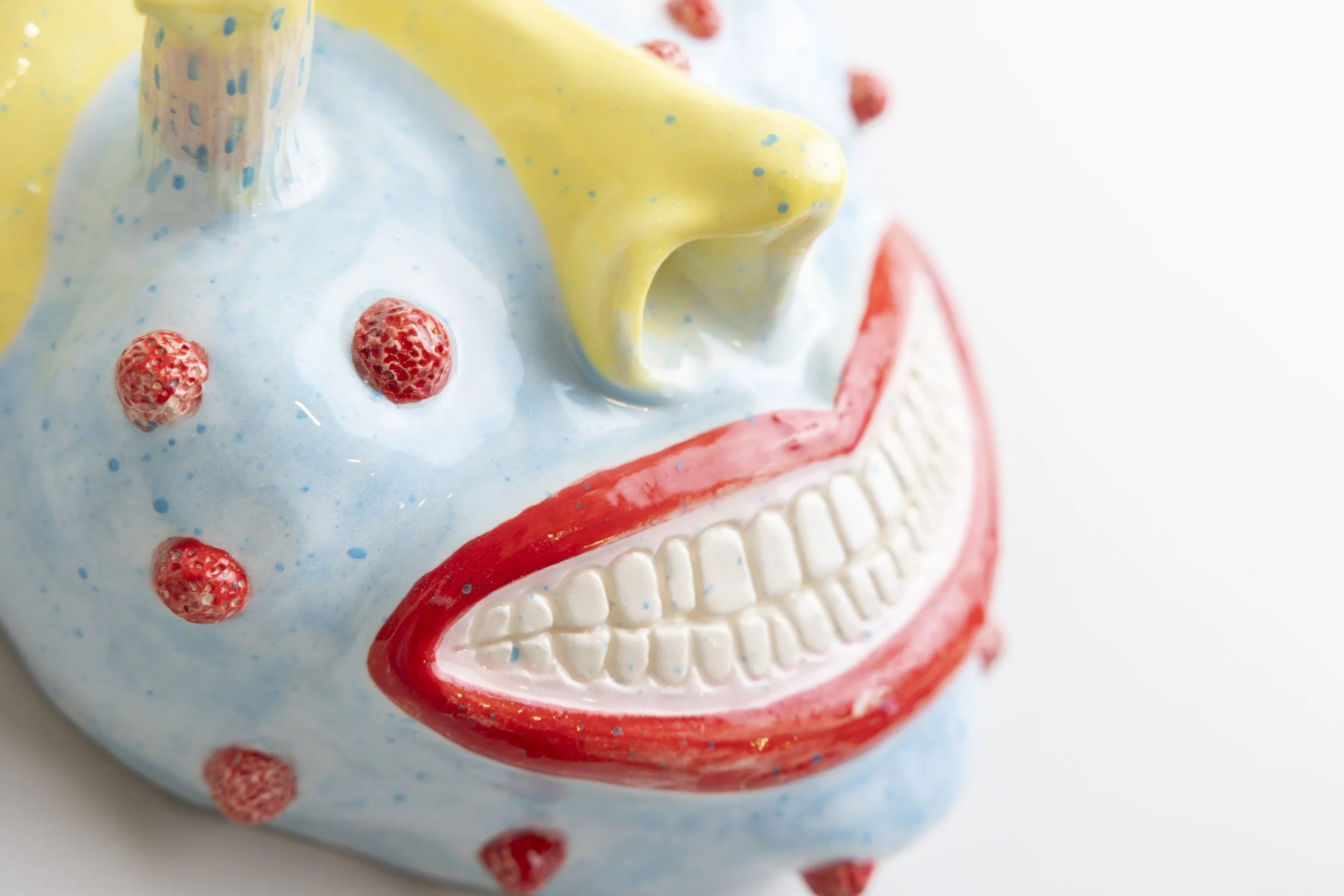 A close-up of a decorative skull with colorful paint, featuring red strawberries on its surface, a yellow 3D-printed horn, and other painted details.