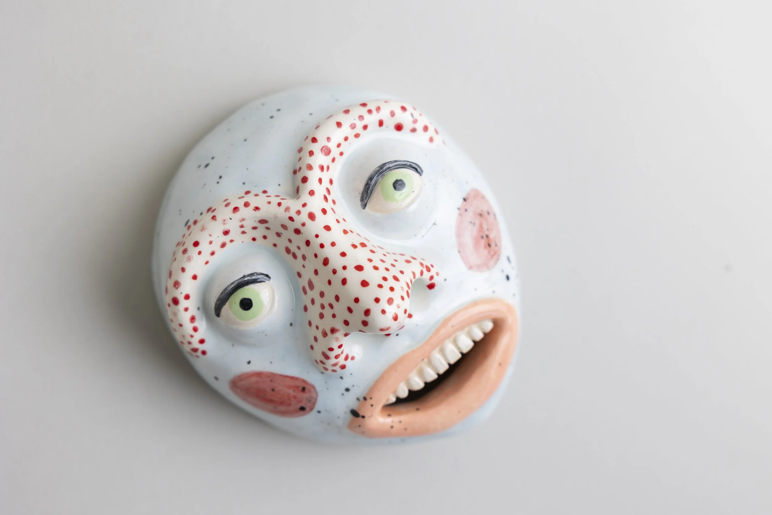 Colorful ceramic skull with painted facial features and red dotted decoration on a light background.