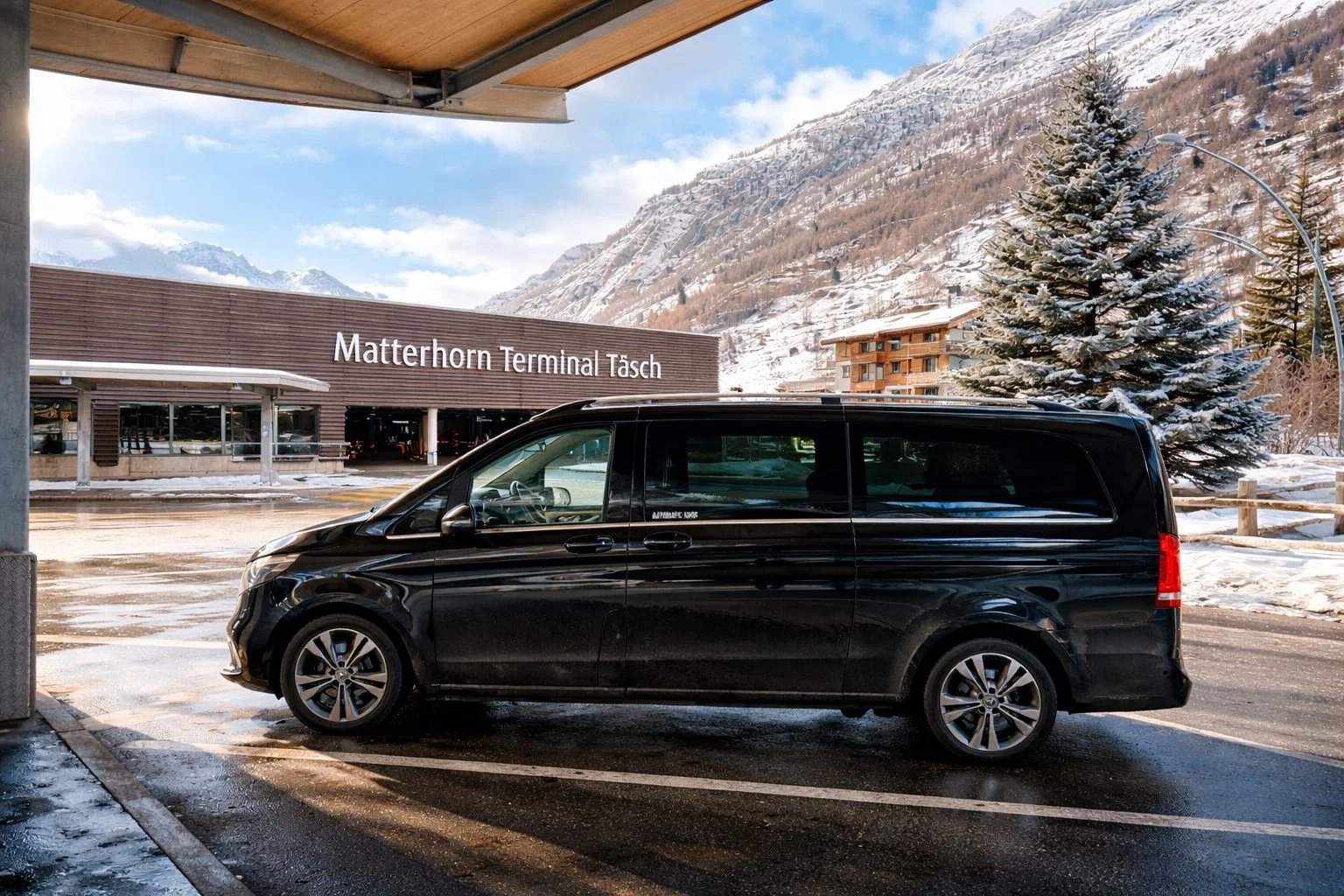 Black van parked outside Matterhorn Terminal Täsch with snow-covered mountains, a pine tree, and buildings in the background.