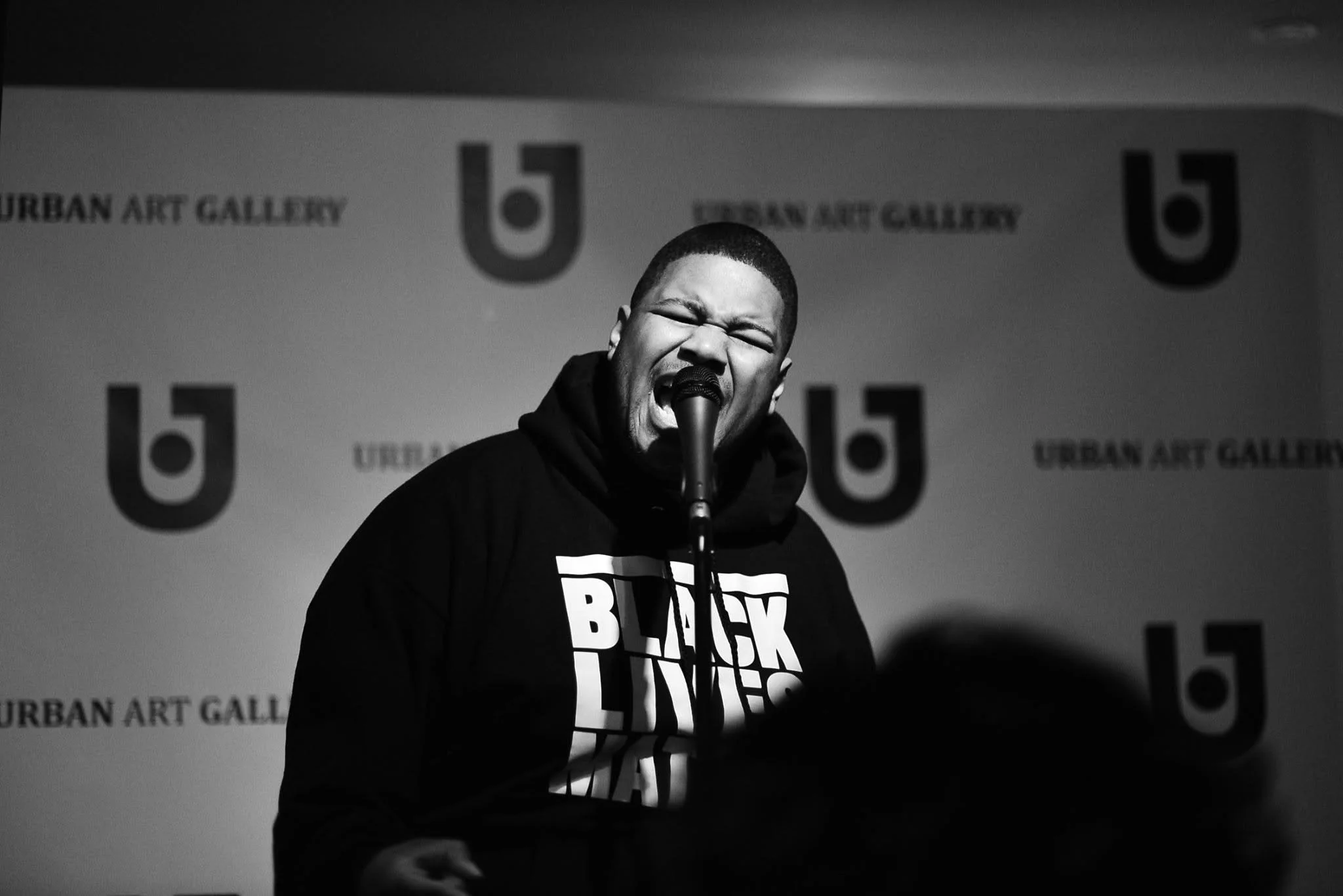 A young black man with a Black Lives Matter hoodie shouting into a mic