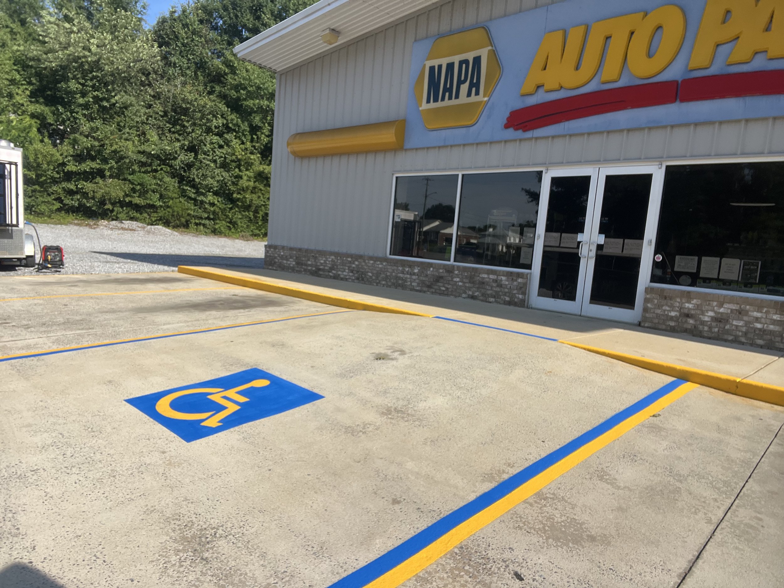 A parking lot with a handicapped parking space and sign in front of a NAPA Auto Parts store.