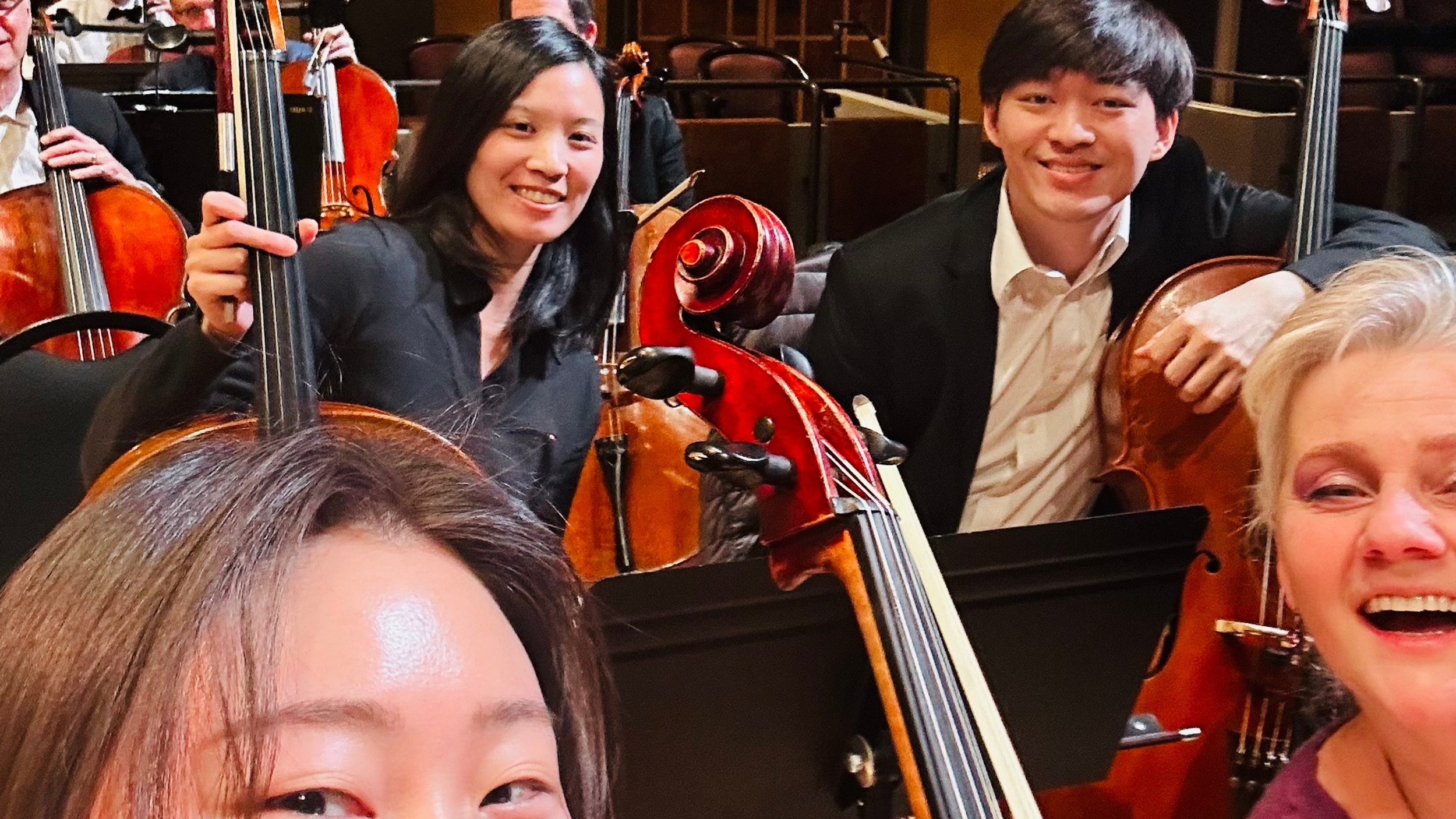 People smiling with string instruments at an orchestra concert.