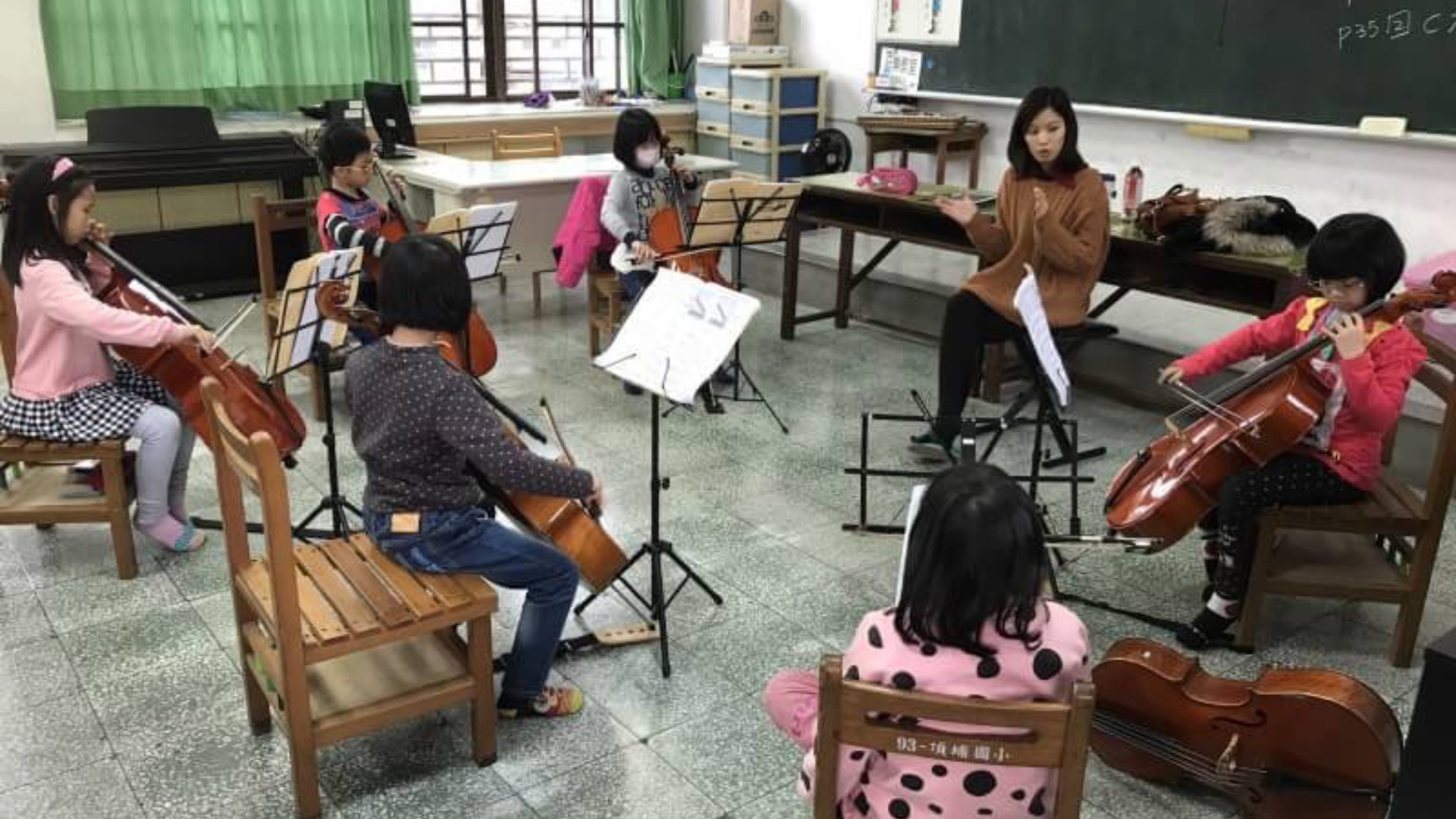 Young children in a classroom practice playing the cello with an instructor.