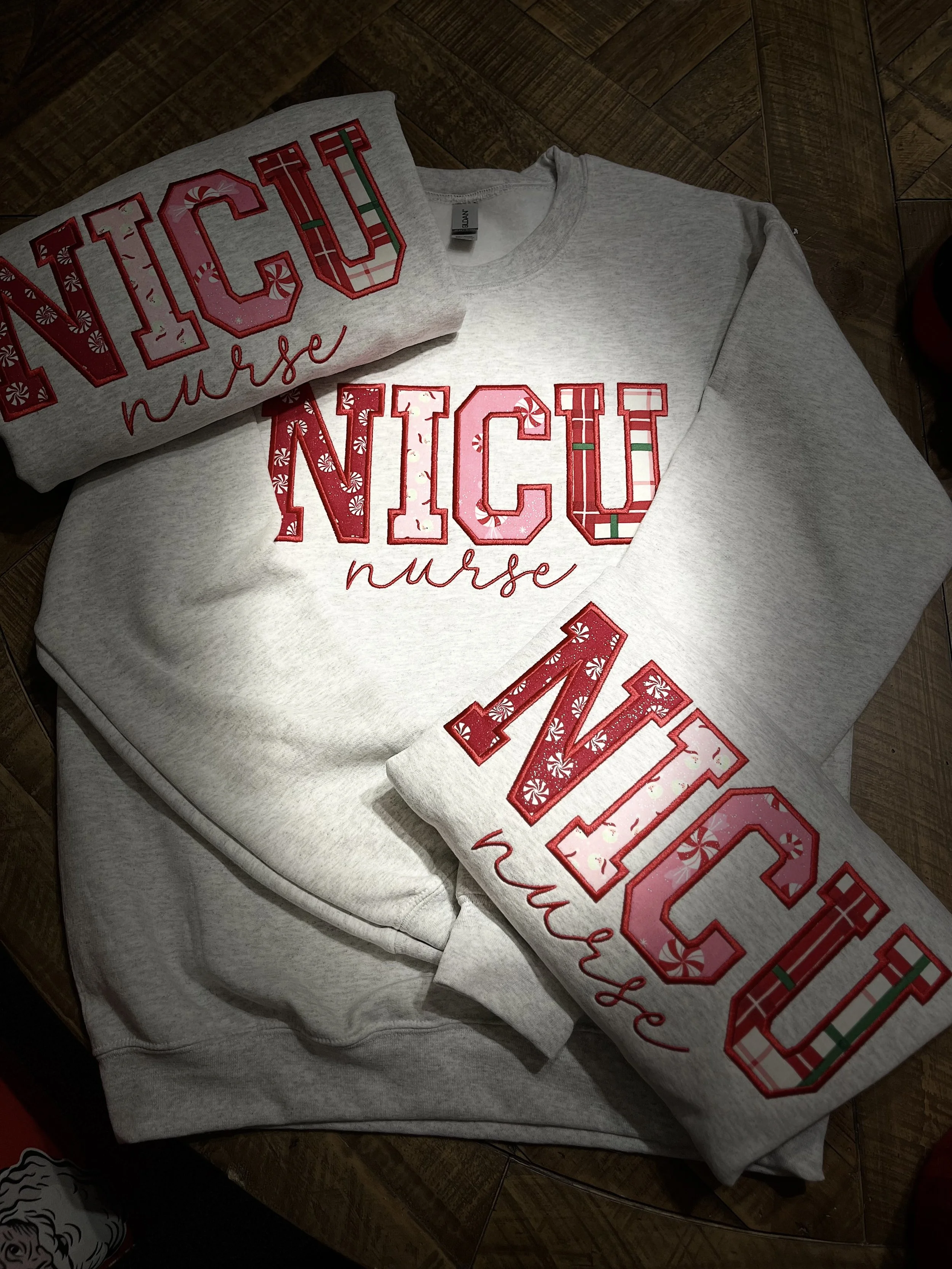 Gray sweatshirt with red embroidered text that reads 'NICOLE nurse' and festive candy cane pattern details.