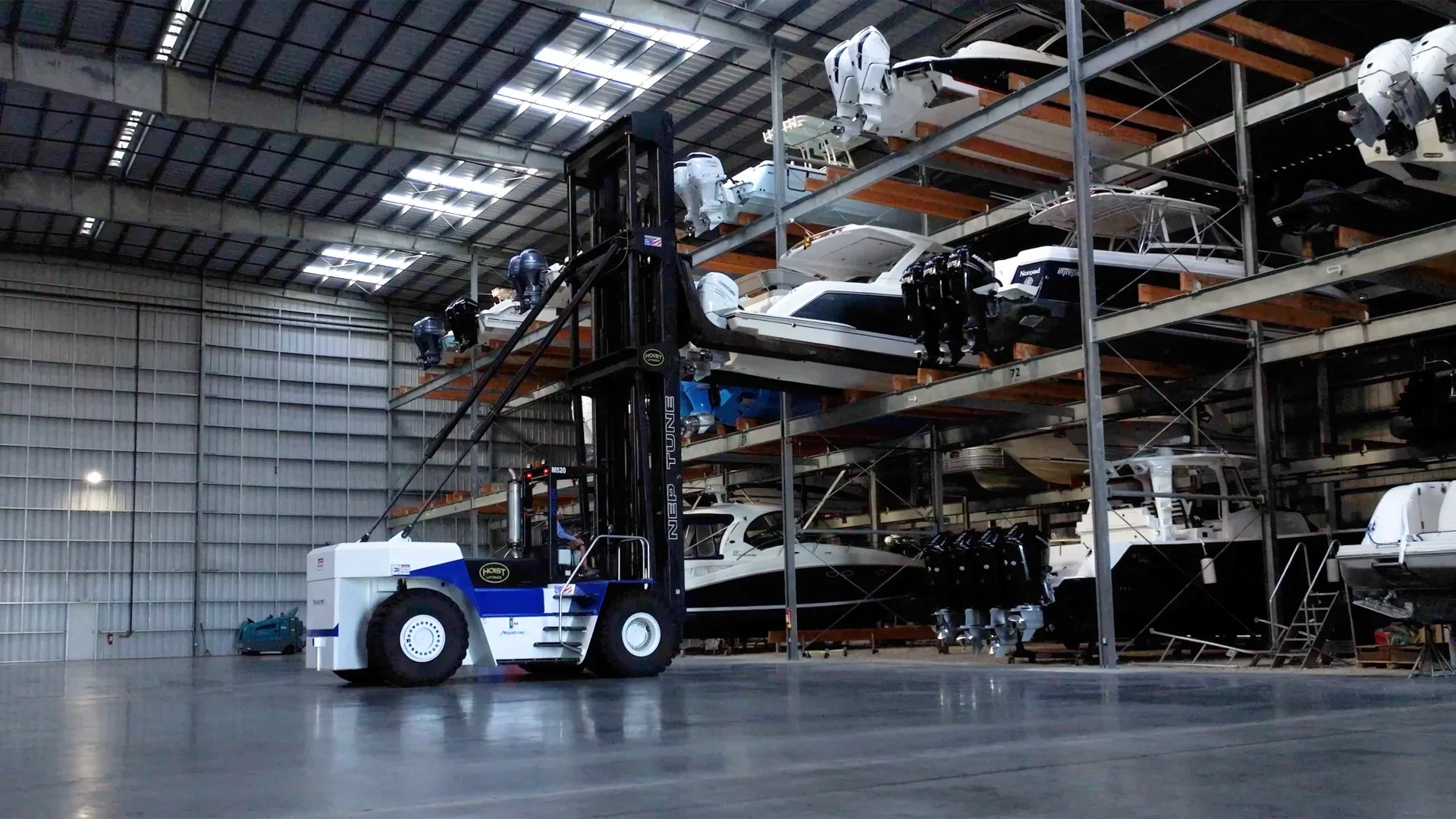 Warehouse with multiple boats stored on metal racks and a forklift moving a boat in the foreground.