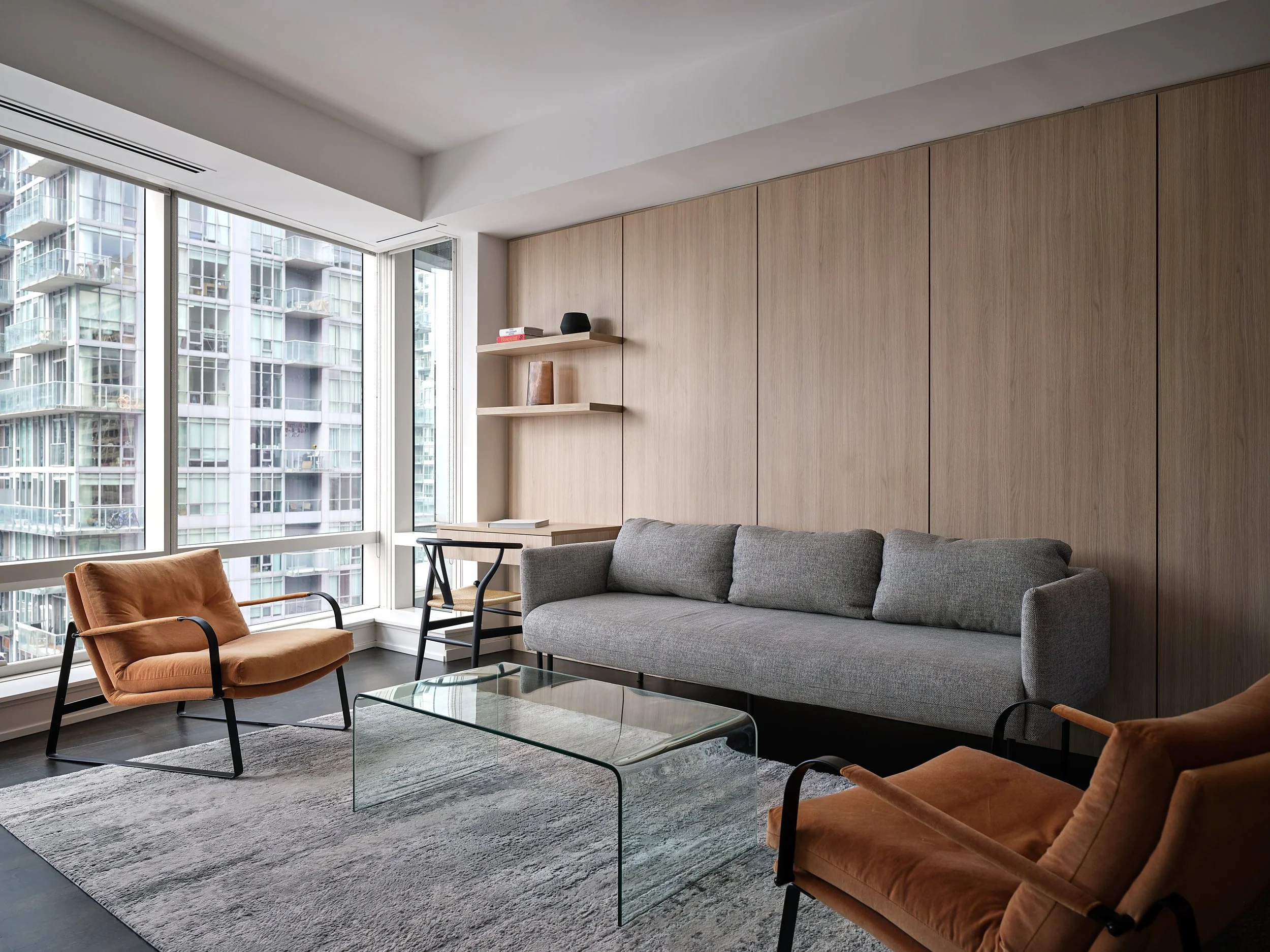 Living room with a full-height white oak panelled wall, floating shelves, and city views.