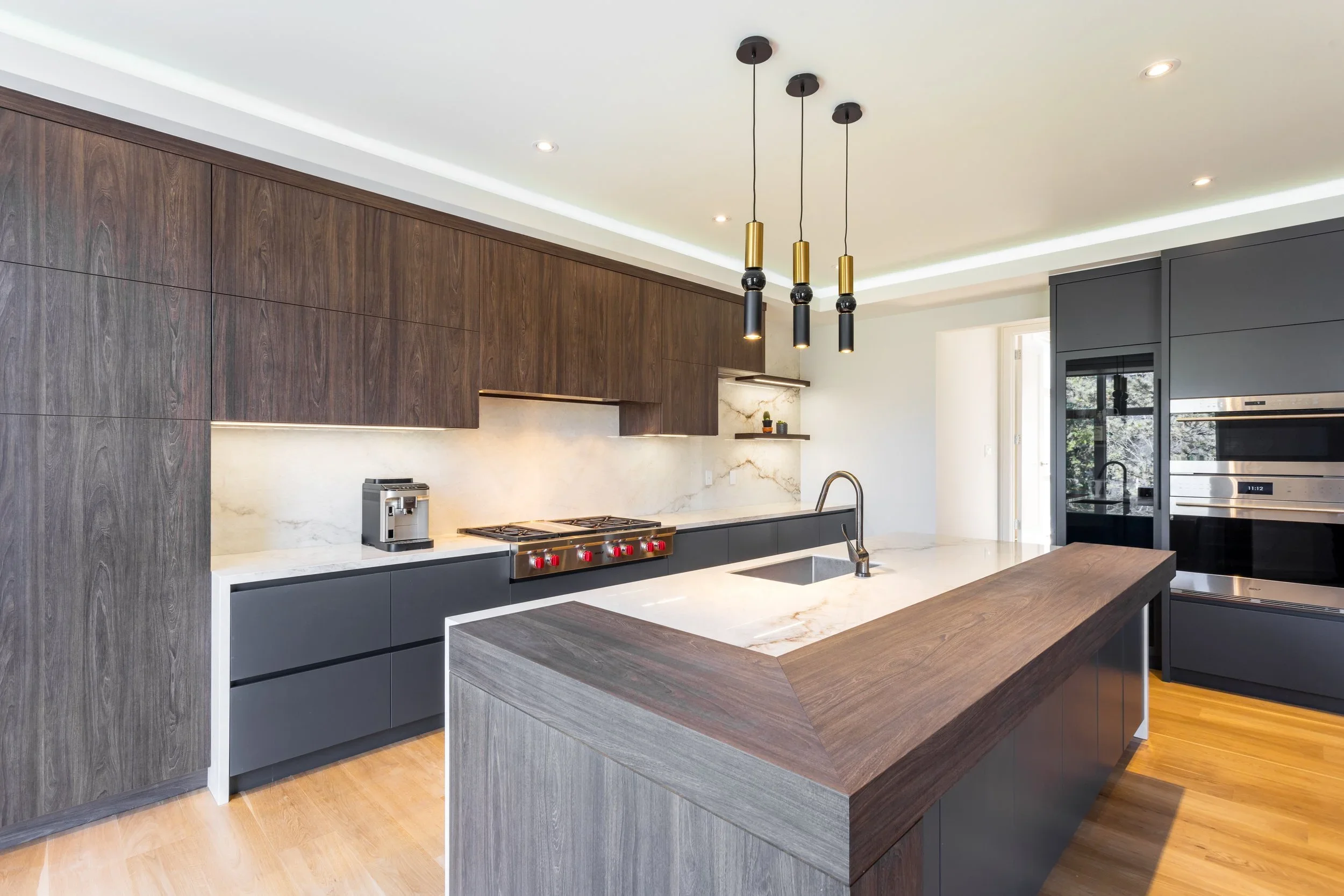 Warm woodgrain and matte charcoal kitchen cabinetry around a walnut-topped island.