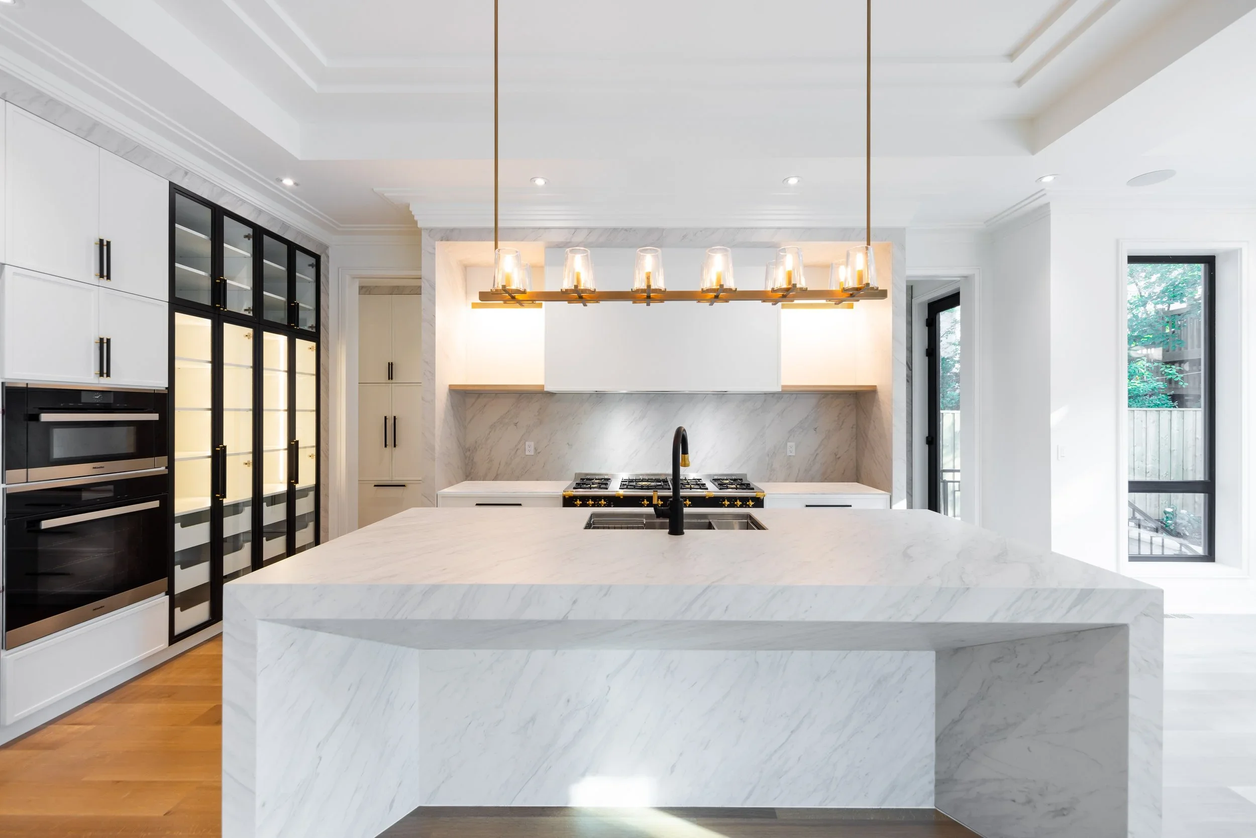 Forest Hill kitchen with a monolithic white stone island, black-framed display cabinetry, and brass lighting.