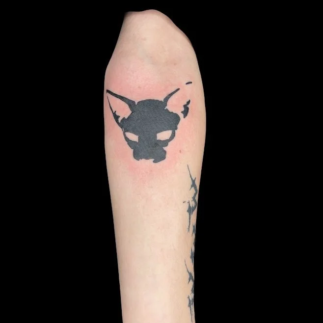 Tattoo of a black skull with bat-like ears on a person's arm.