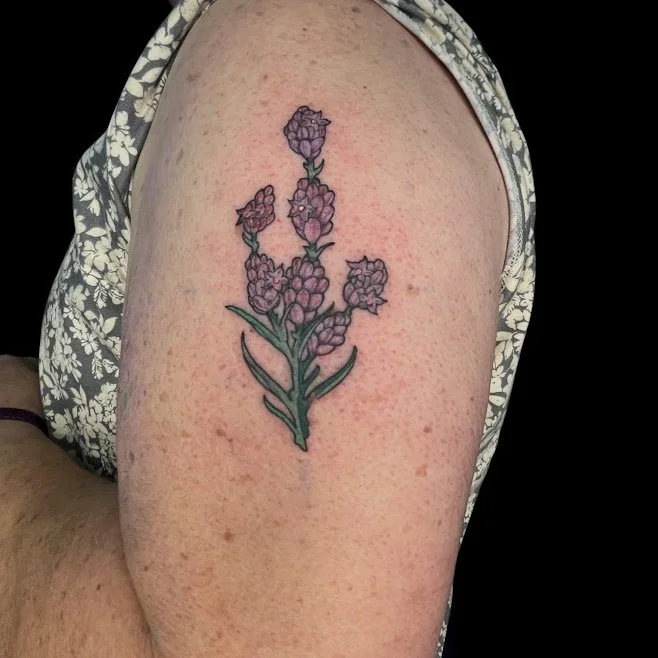 Tattoo of purple lavender flowers and green leaves on upper arm.