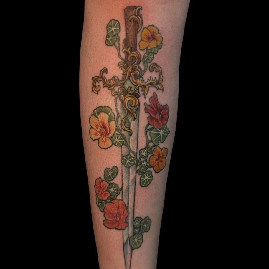Tattoo of a dagger intertwined with orange and yellow hibiscus flowers and green leaves.