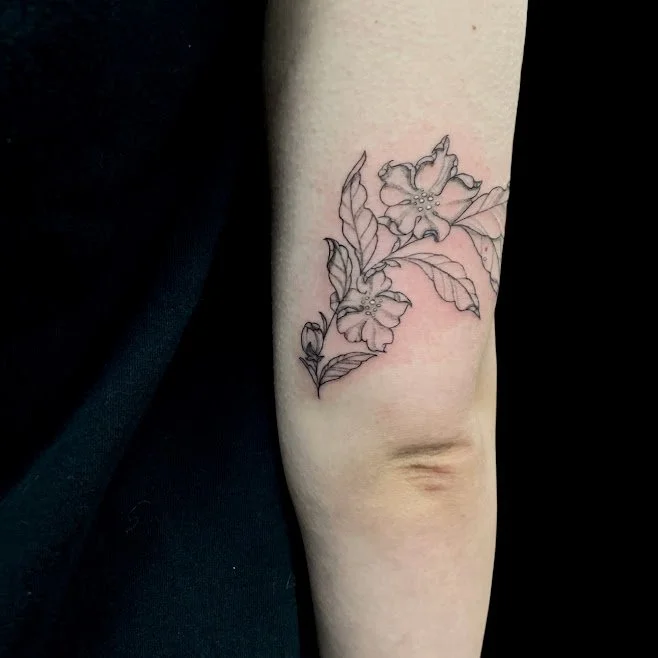 Black outline floral tattoo on the upper arm featuring two flowers and leaves.