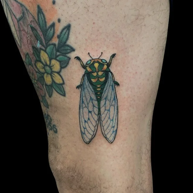 Tattoo of a cicada on a person's thigh, with flowers partially visible nearby.
