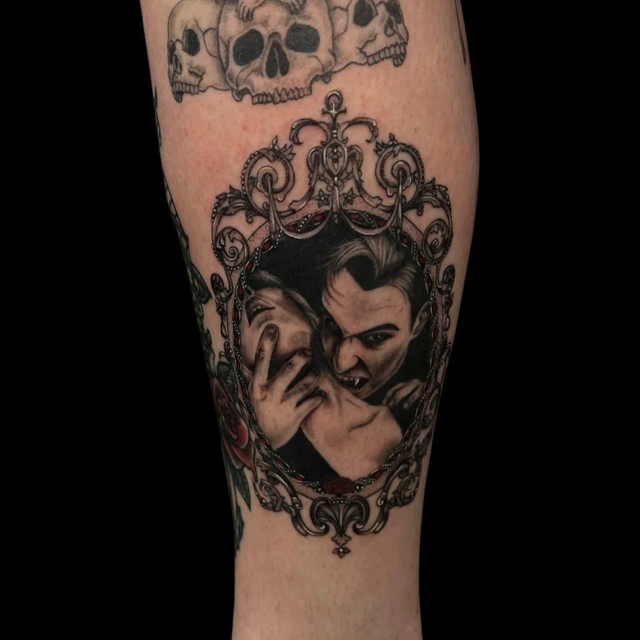Tattoo of two men within an ornate, decorative frame. One man is grinning and showing a fang, while the other is covering his face with his hand.