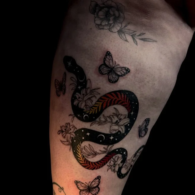 Tattoo of a colorful snake intertwined with flowers and butterflies on the person's thigh.