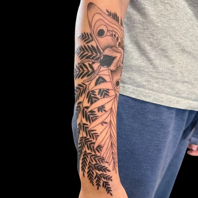 Black and gray tattoo of abstract leaves and foliage extending down a person's arm.
