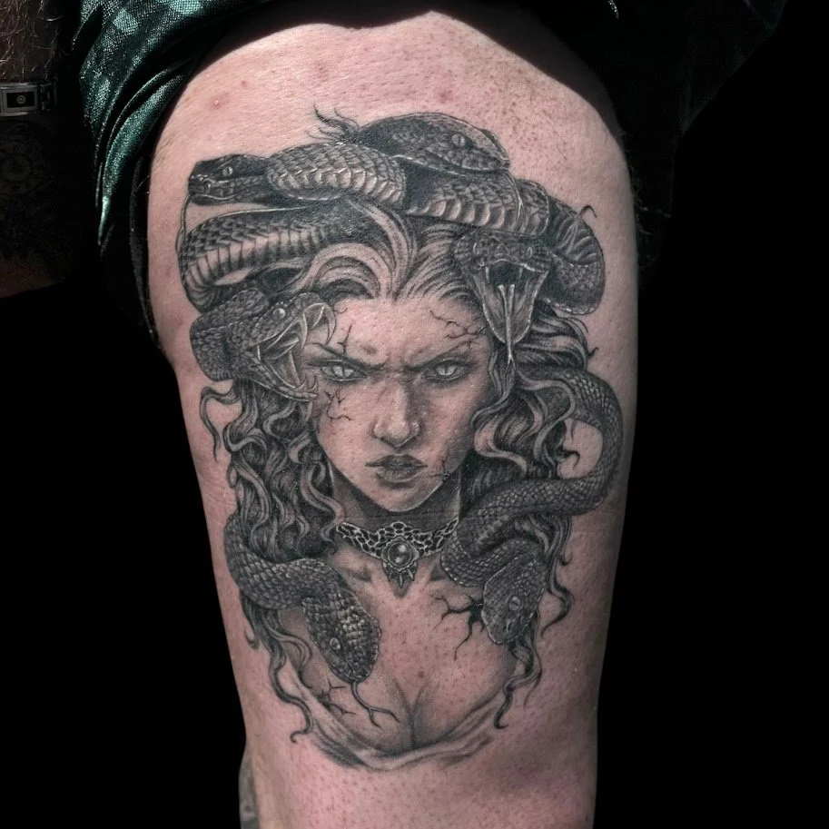 Tattoo of a woman with serpents in her hair and a snake on her shoulder, with a fierce expression.